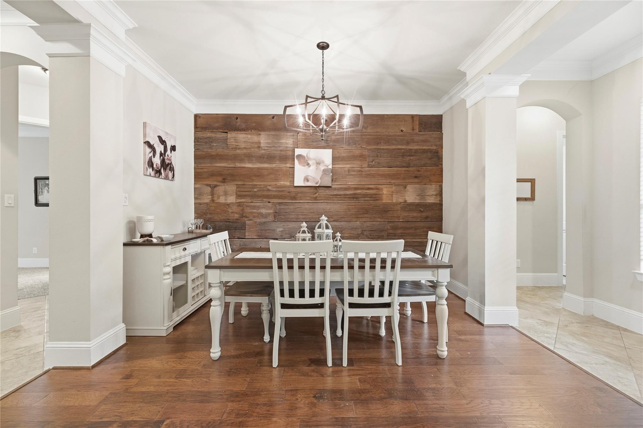 Dining room with a rustic wood-plank accent wall, white table and chairs, and a geometric pendant light.