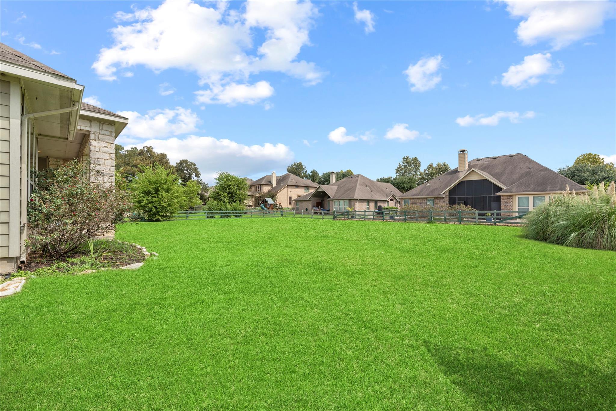 Spacious green backyard lawn with a low fence, landscaped edges, and neighboring homes beyond.