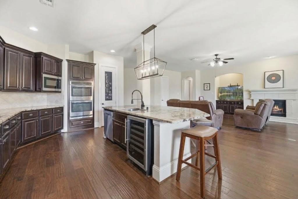 Open kitchen with a large stone island, dark wood cabinetry, and an adjoining living room with a fireplace.