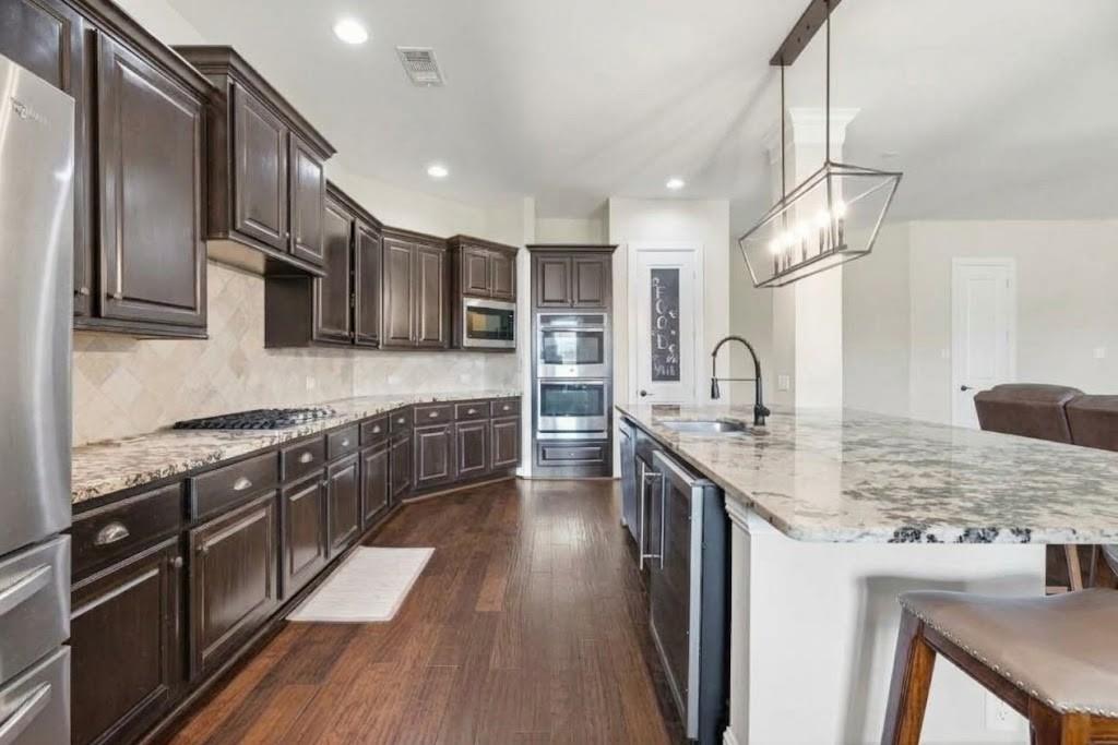 Kitchen with dark wood cabinets, stainless steel appliances, and a large granite island with sink.