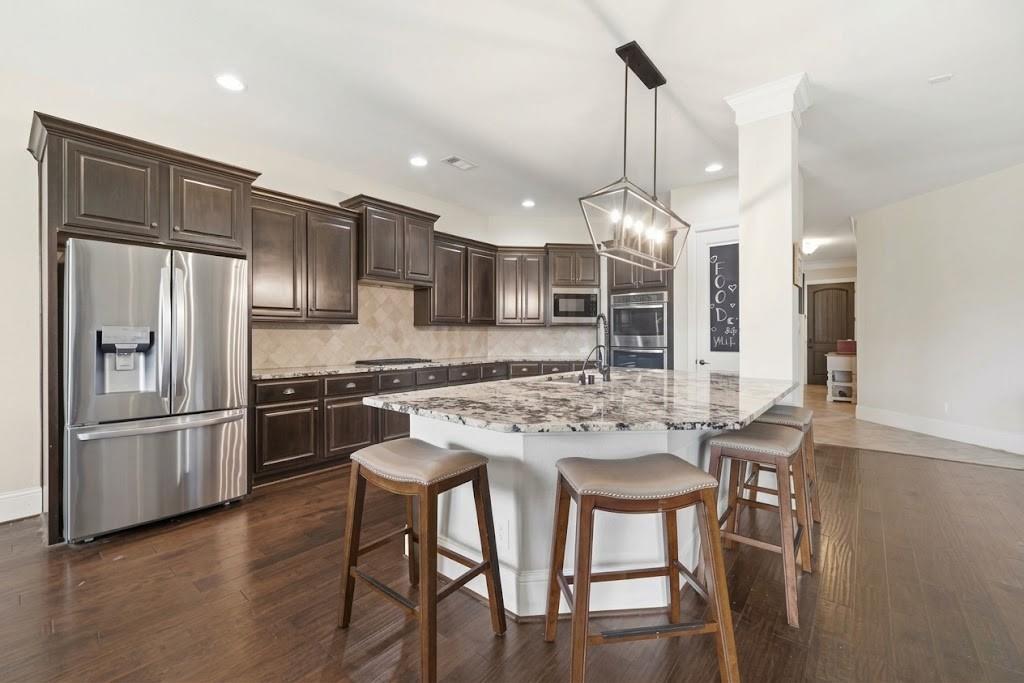 Kitchen with dark wood cabinets, stainless steel appliances, and a large granite island with bar stools.