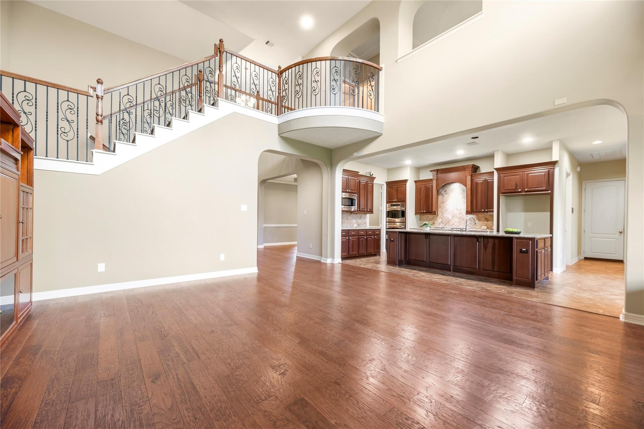 Open living area with hardwood floors, curved staircase, and adjoining kitchen with dark wood cabinets.
