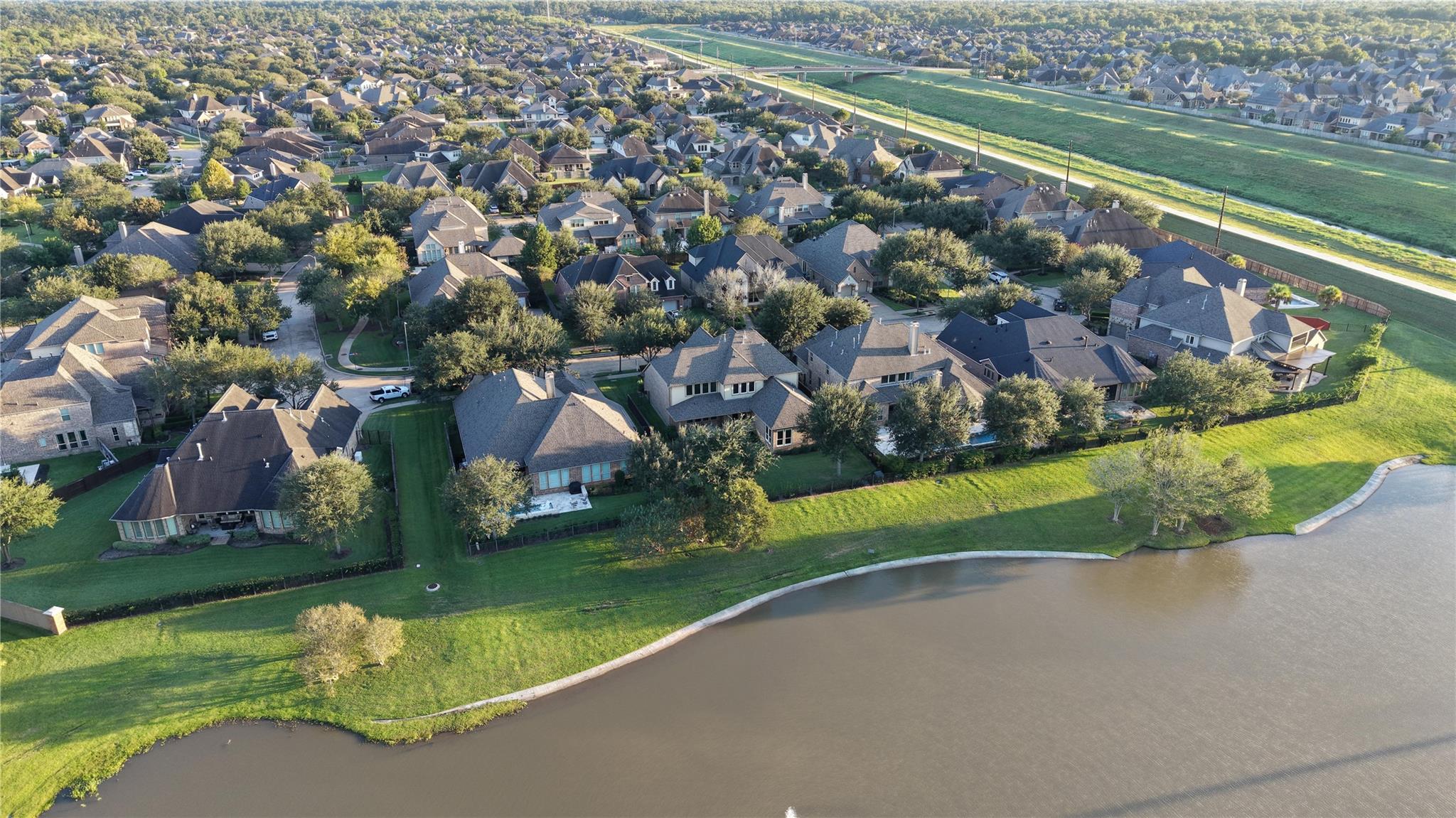 Aerial view of homes beside a pond, with a green corridor and tree-lined streets beyond.