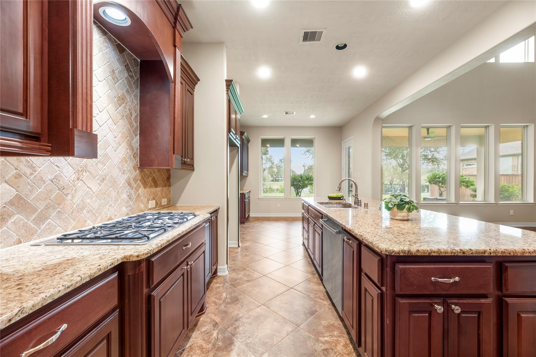 Kitchen with cherry cabinets, granite island, gas cooktop, and tall windows.