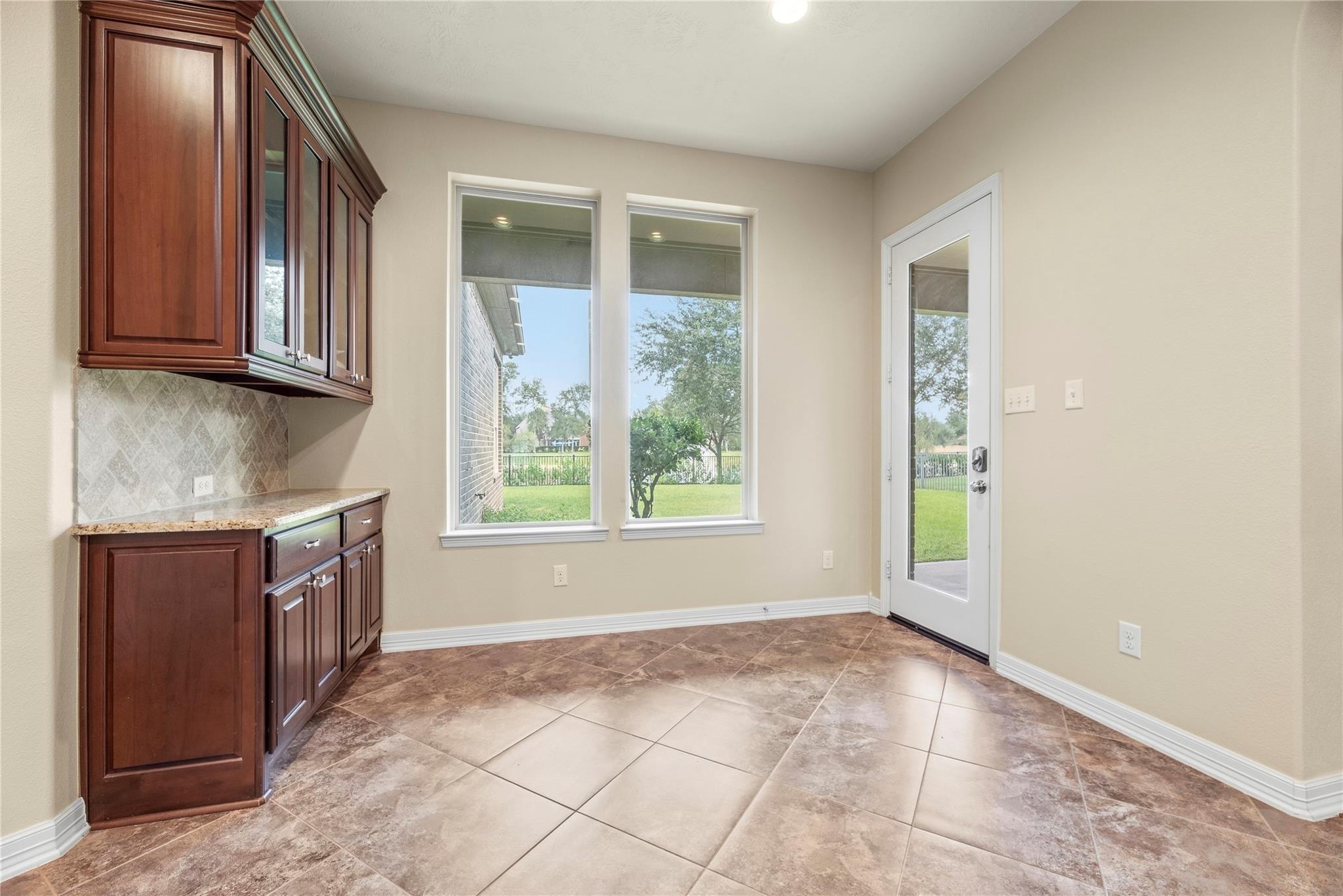 Empty room with dark wood cabinets, large tile flooring, and windows overlooking the lawn.