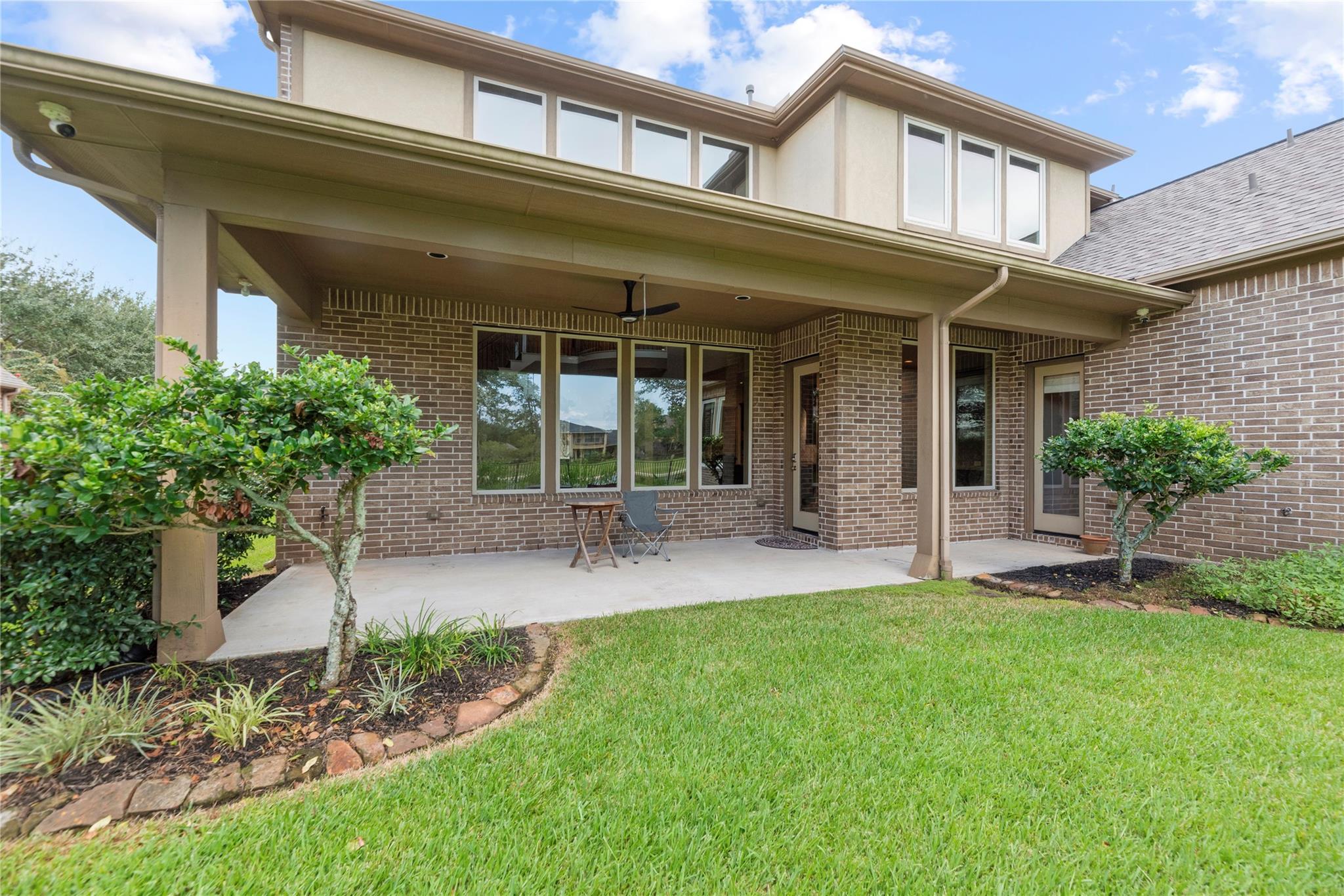 Two-story brick home with a covered backyard patio, ceiling fan, and landscaped lawn.