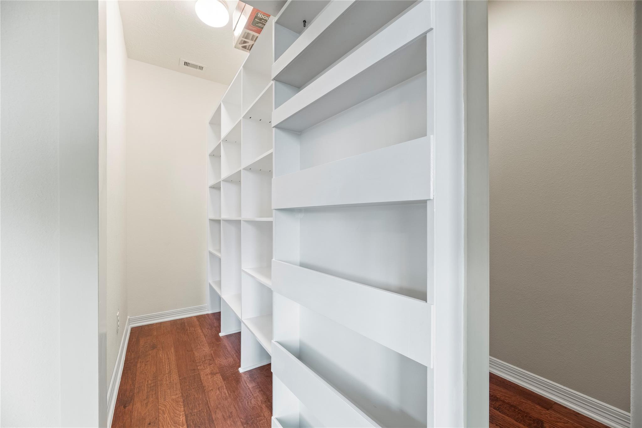 Empty room with floor-to-ceiling white built-in shelving and reddish-brown wood flooring.