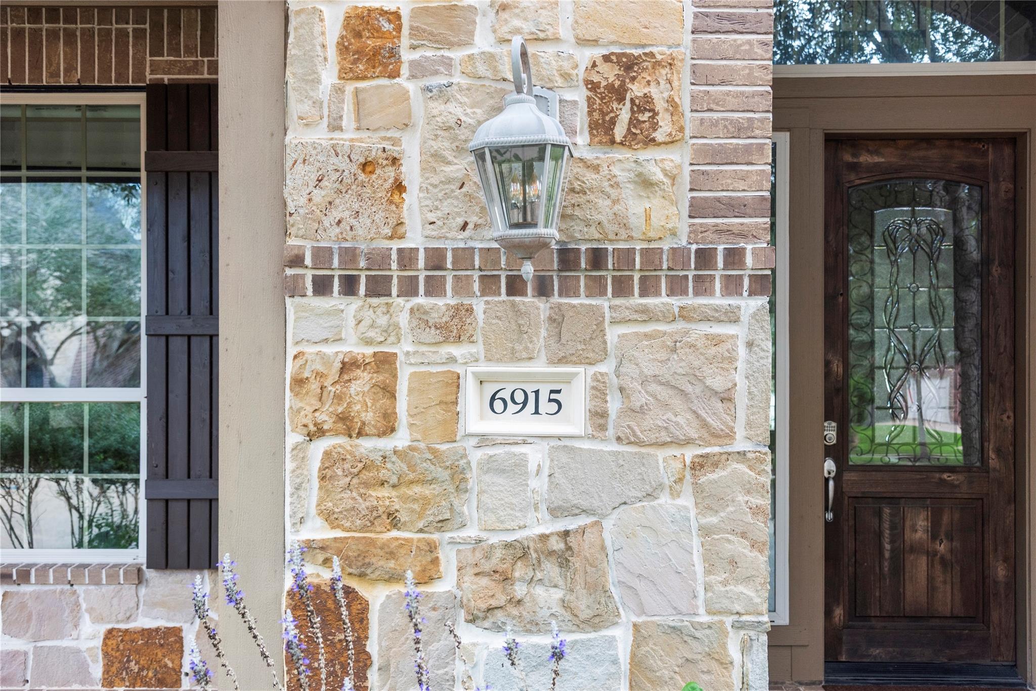 Stone home entrance with a dark wood door, decorative glass, and address plaque 6915.