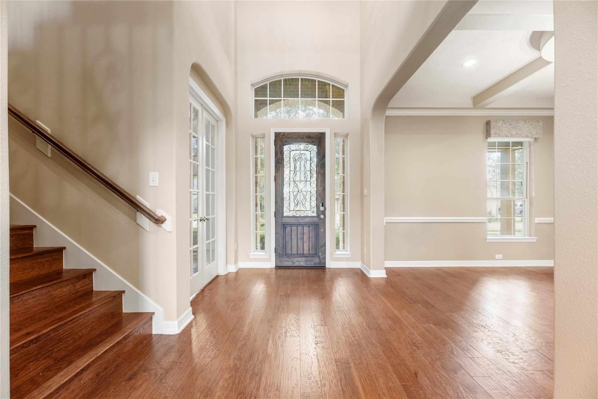 Foyer with a decorative glass front door, tall arched window, wood floors, and staircase.