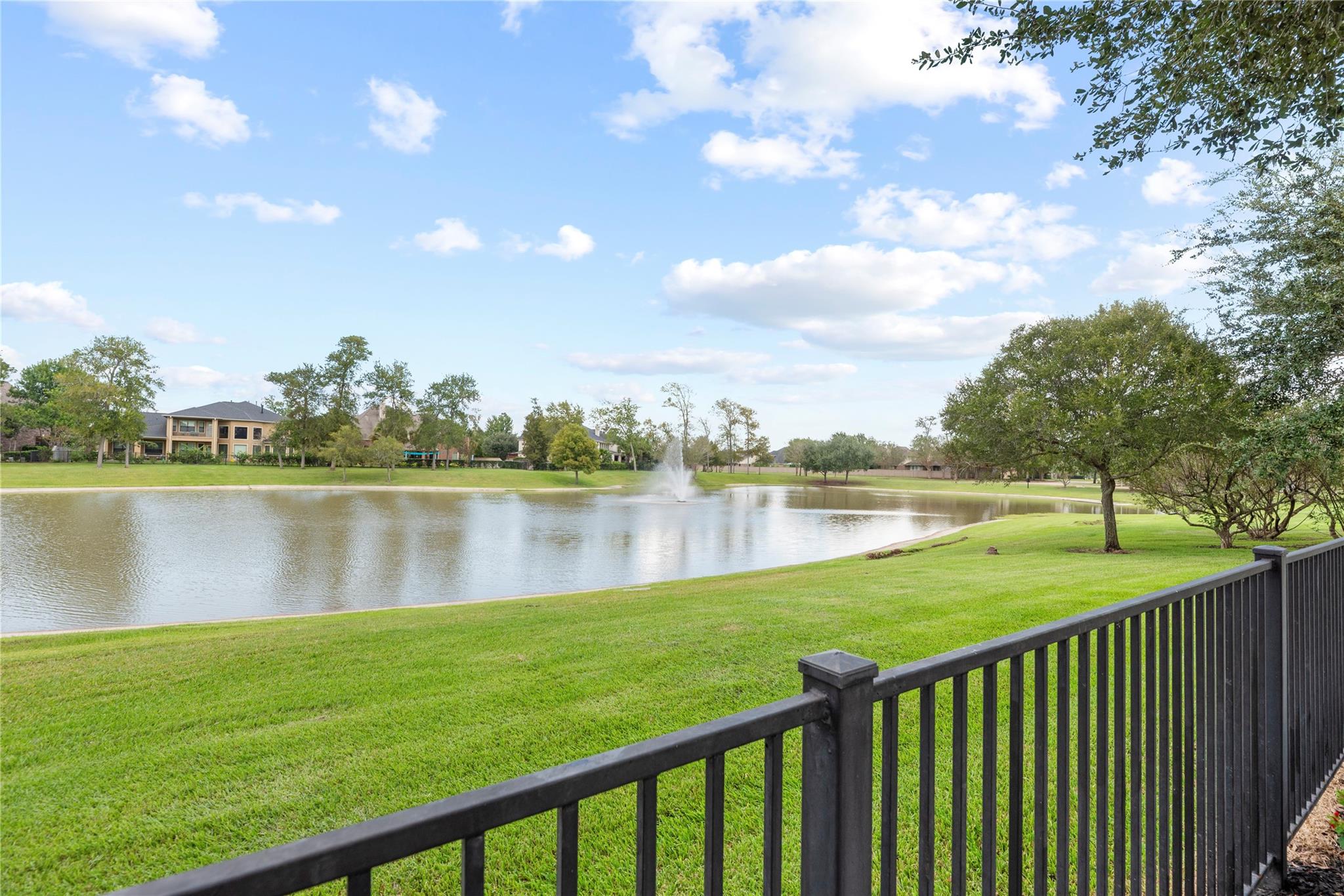 Landscaped pond and fountain beyond a green lawn, viewed over a black railing.