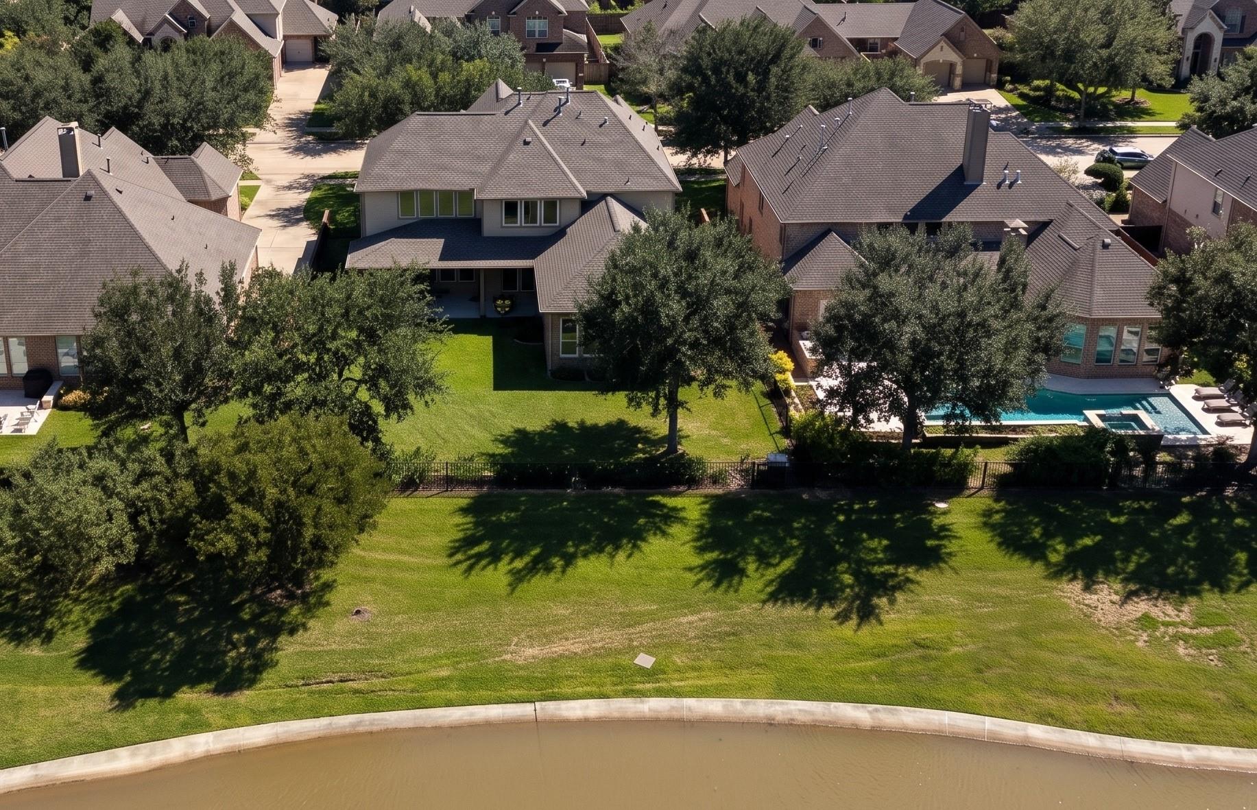 Aerial view of a brick home’s tree-shaded backyard, swimming pool, and adjacent canal.