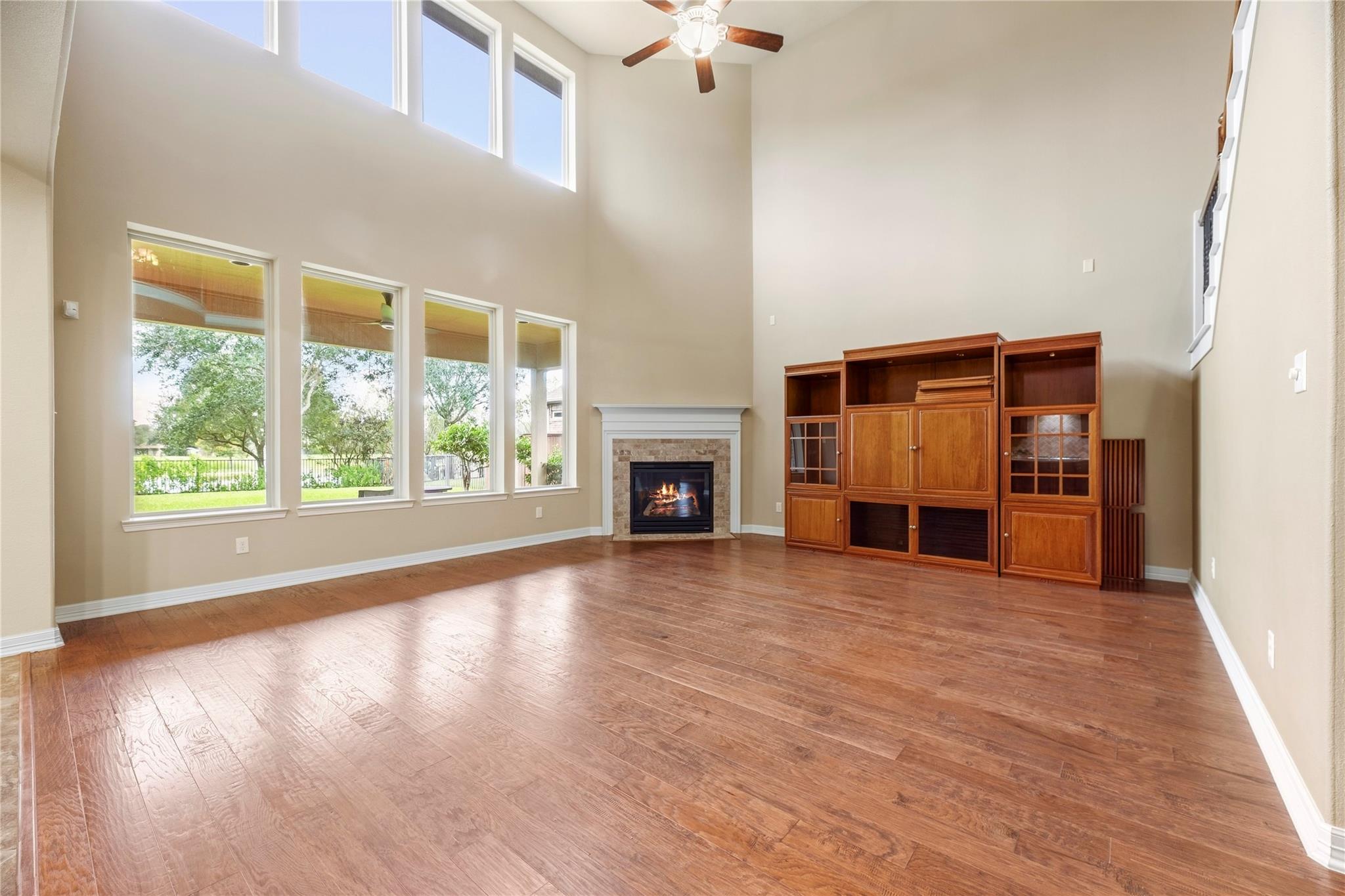 Double-height living room with tall windows, wood floors, a fireplace, and built-in cabinetry.