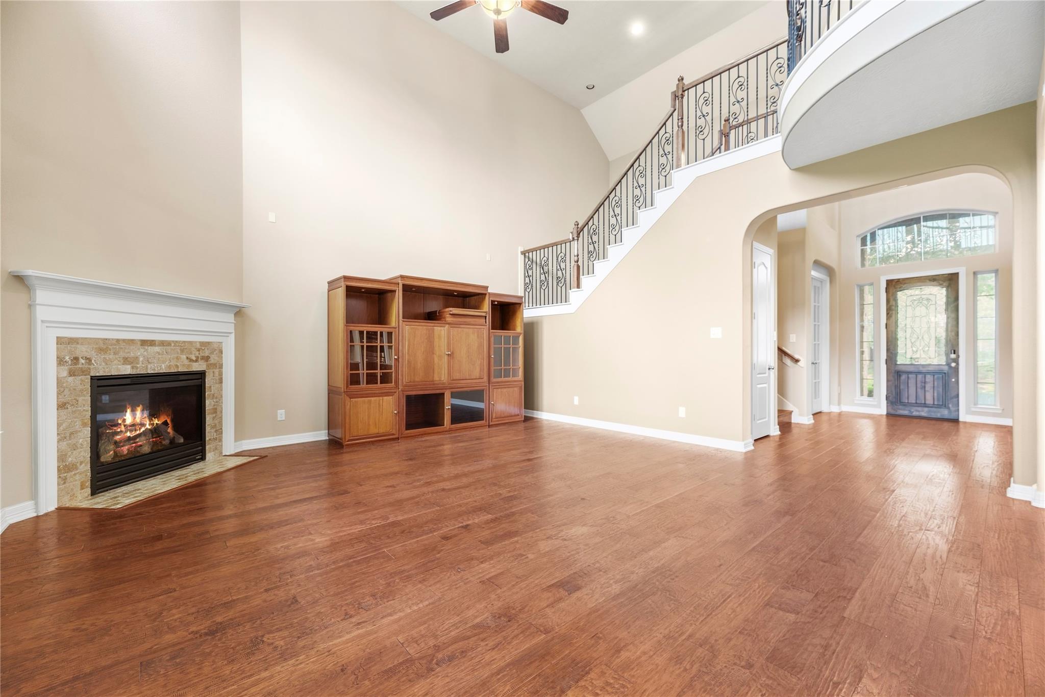 Two-story living room with hardwood floors, stone fireplace, built-in cabinetry, and curved staircase.