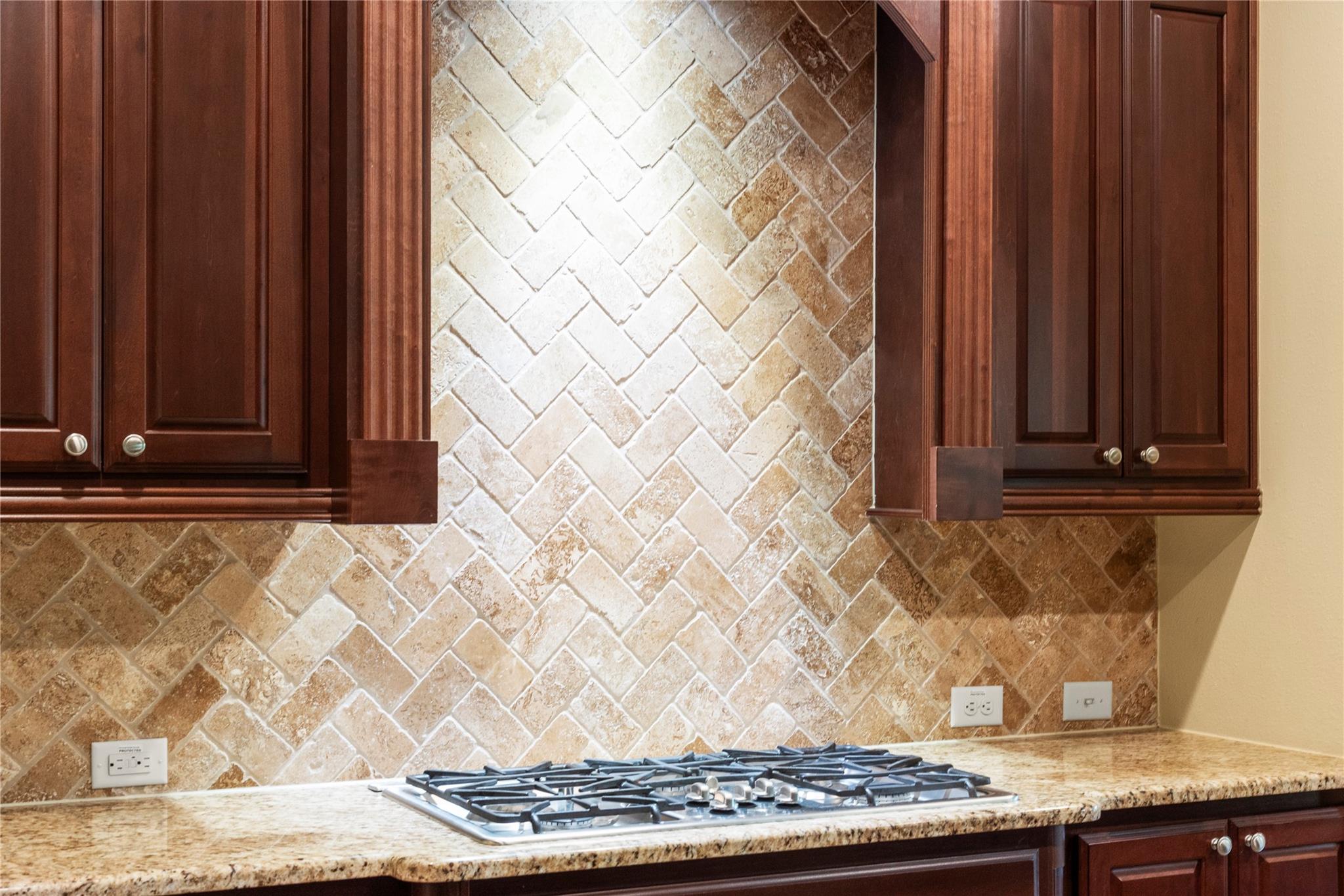 Kitchen with a gas cooktop, granite counters, and tan stone tile backsplash.