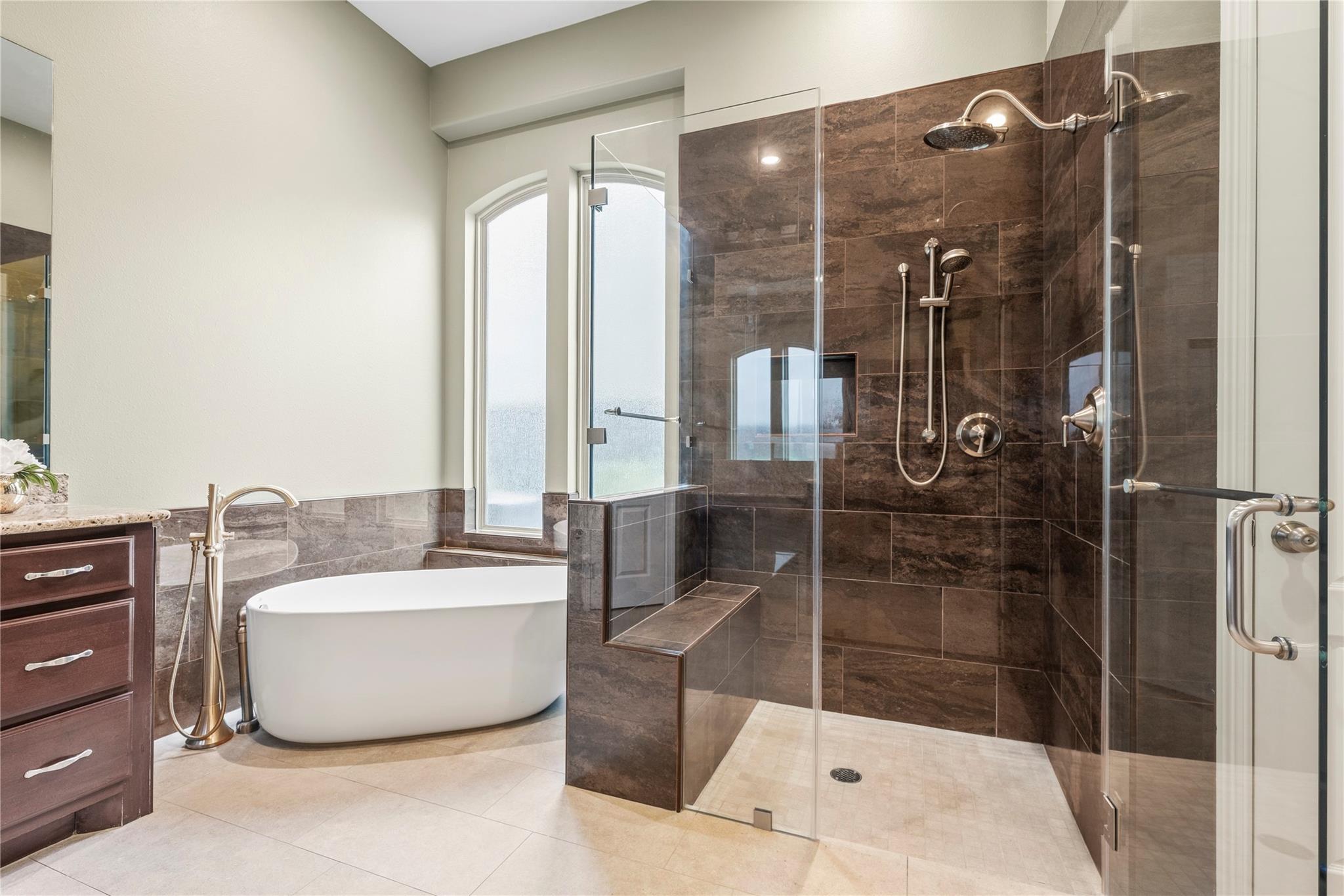 Bathroom with a freestanding soaking tub and dark-tiled glass shower with built-in bench.
