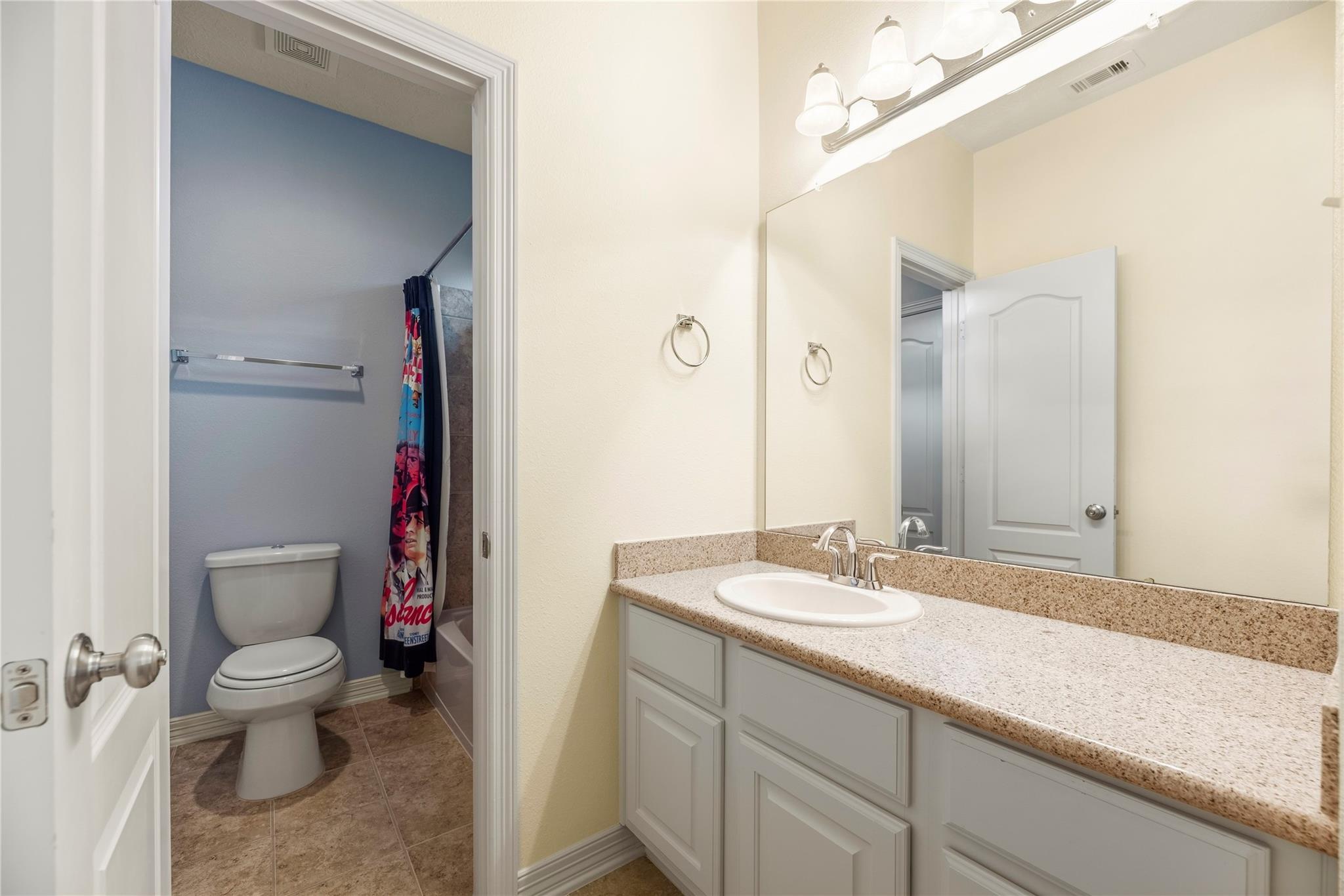 Bathroom vanity with a wide speckled countertop, mirrored wall, and adjoining toilet and shower area.