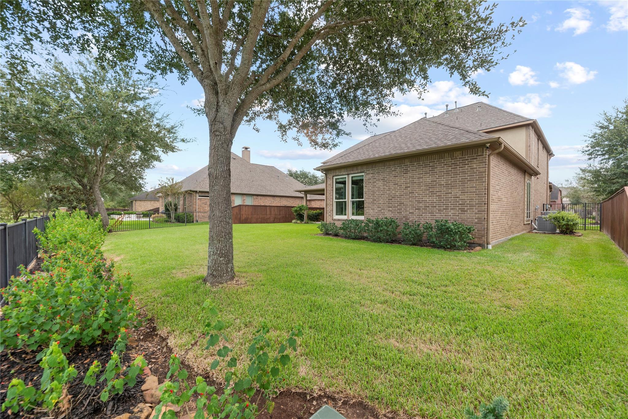 Two-story brick home behind a broad lawn and mature shade tree.