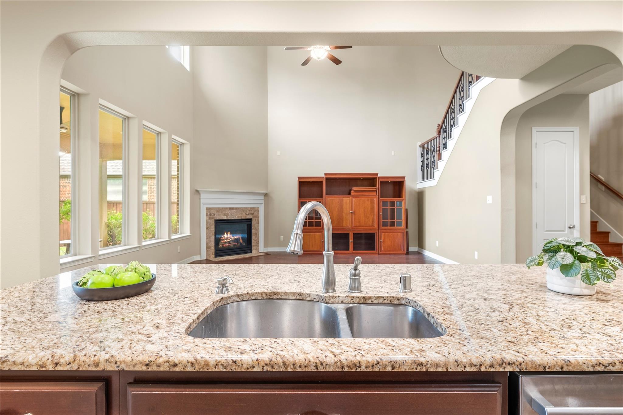 Kitchen island and sink overlooking a high-ceilinged living room with a fireplace and staircase.
