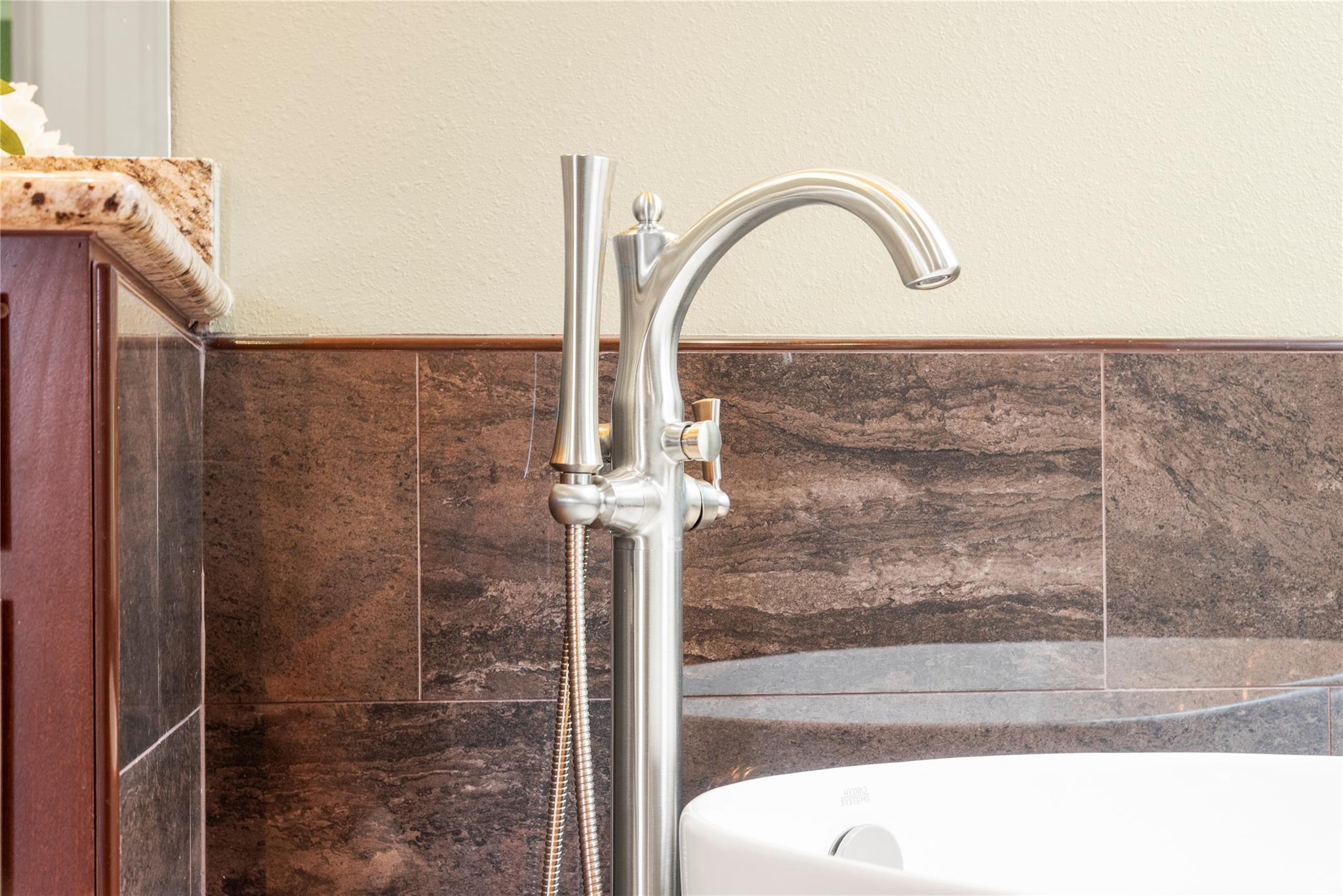 Freestanding bathtub with a polished floor-mounted faucet against dark stone tile.