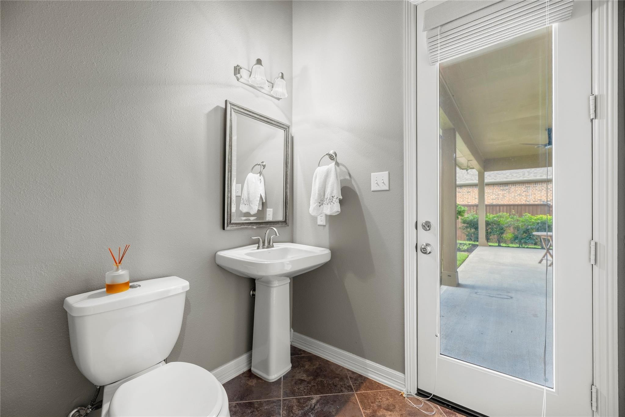 Bathroom with a pedestal sink and toilet beside a glass door opening to a covered patio.