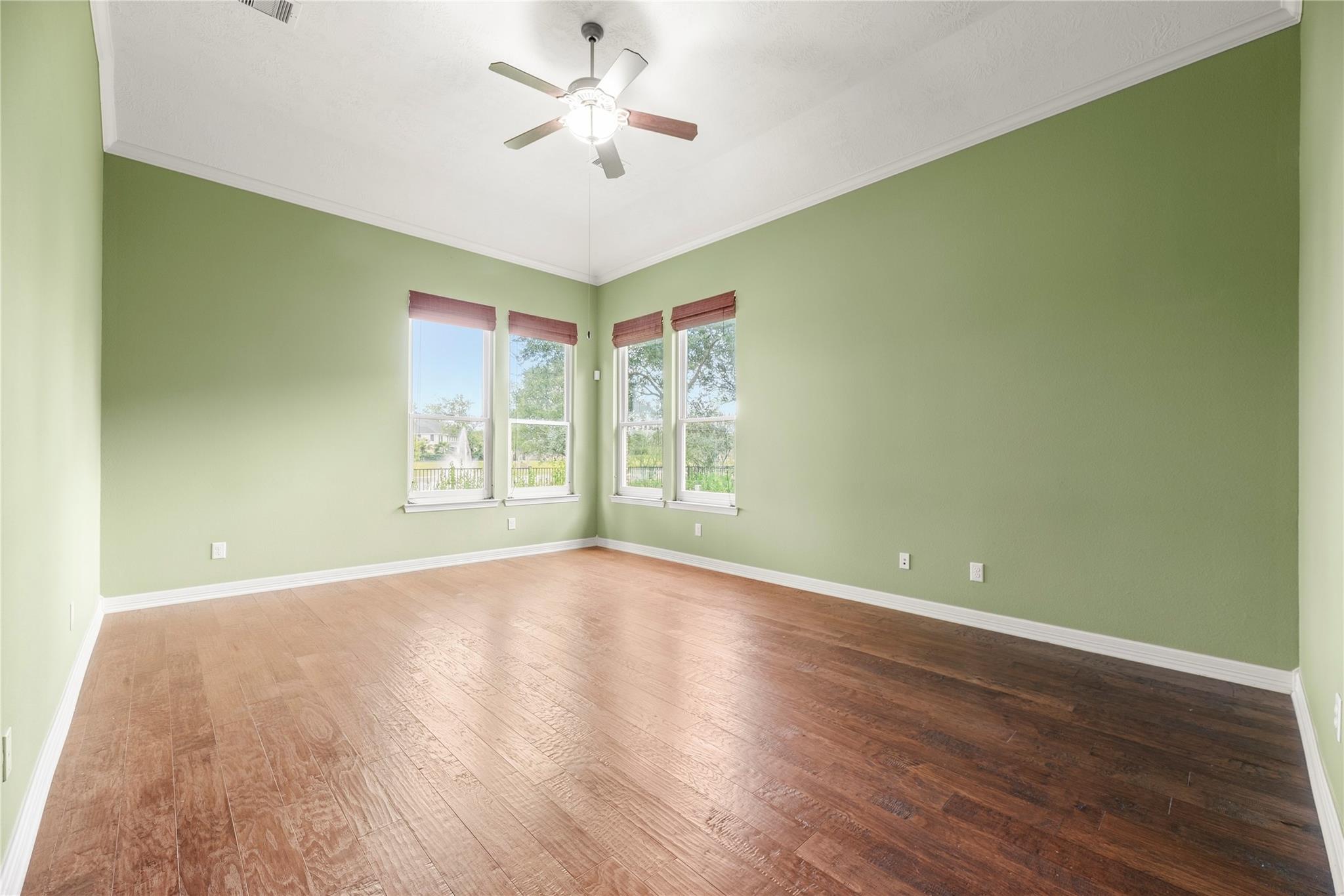 Empty room with green walls, hardwood floors, four windows, and a ceiling fan.