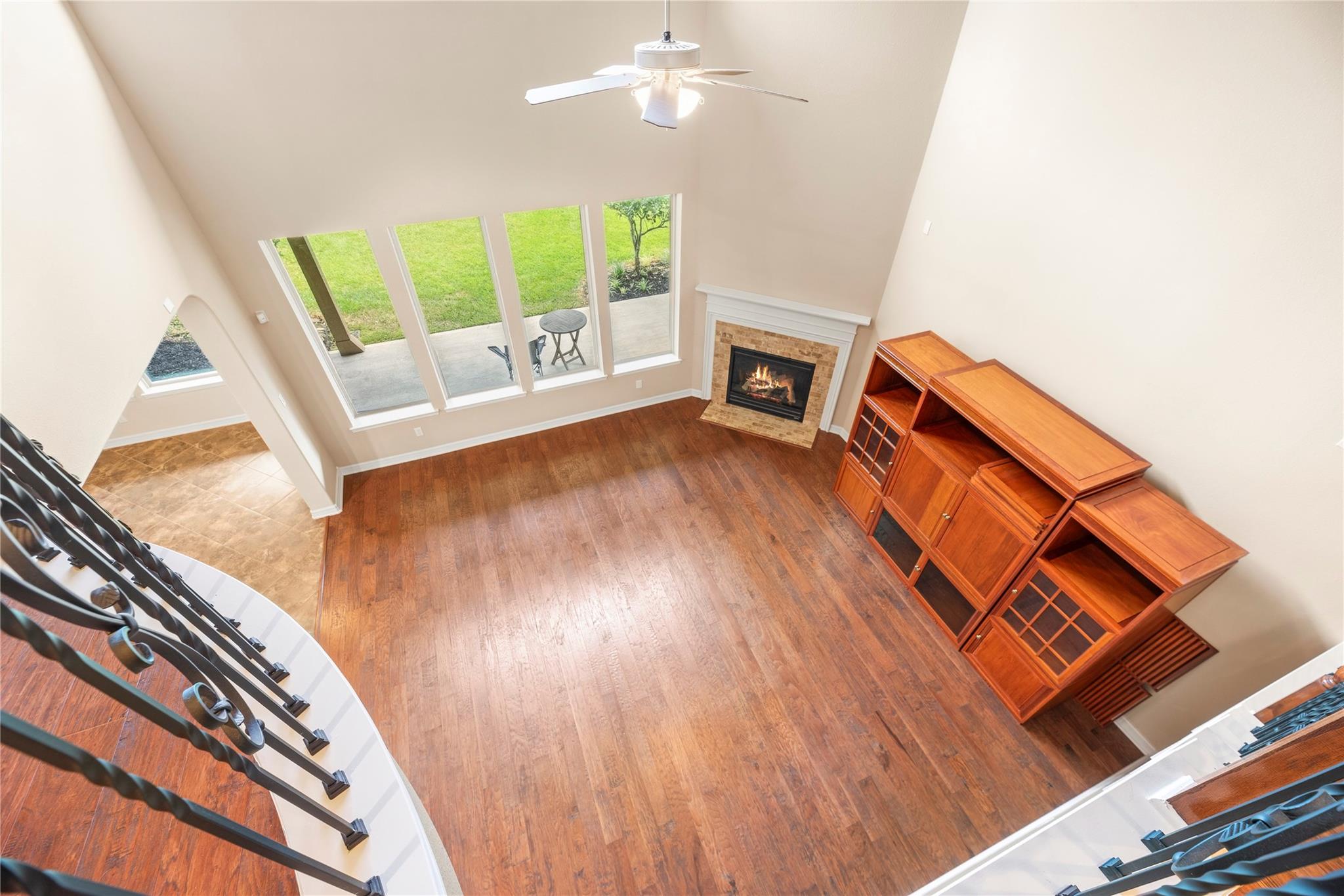 Two-story living room with hardwood floors, a stone fireplace, tall patio-facing windows, and a built-in wooden entertainment center.