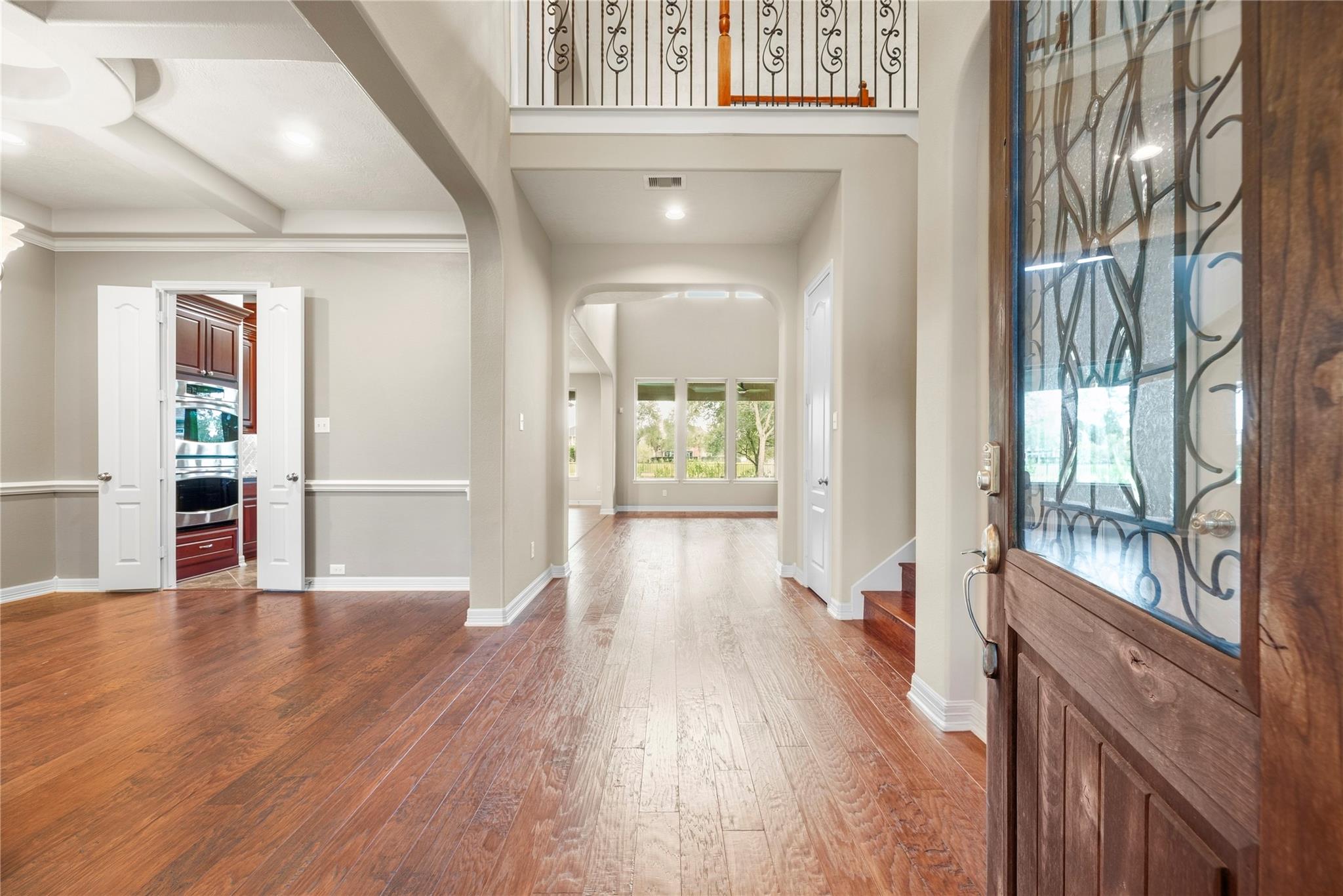Home entry with decorative glass front door, wood floors, open kitchen, and upstairs landing.
