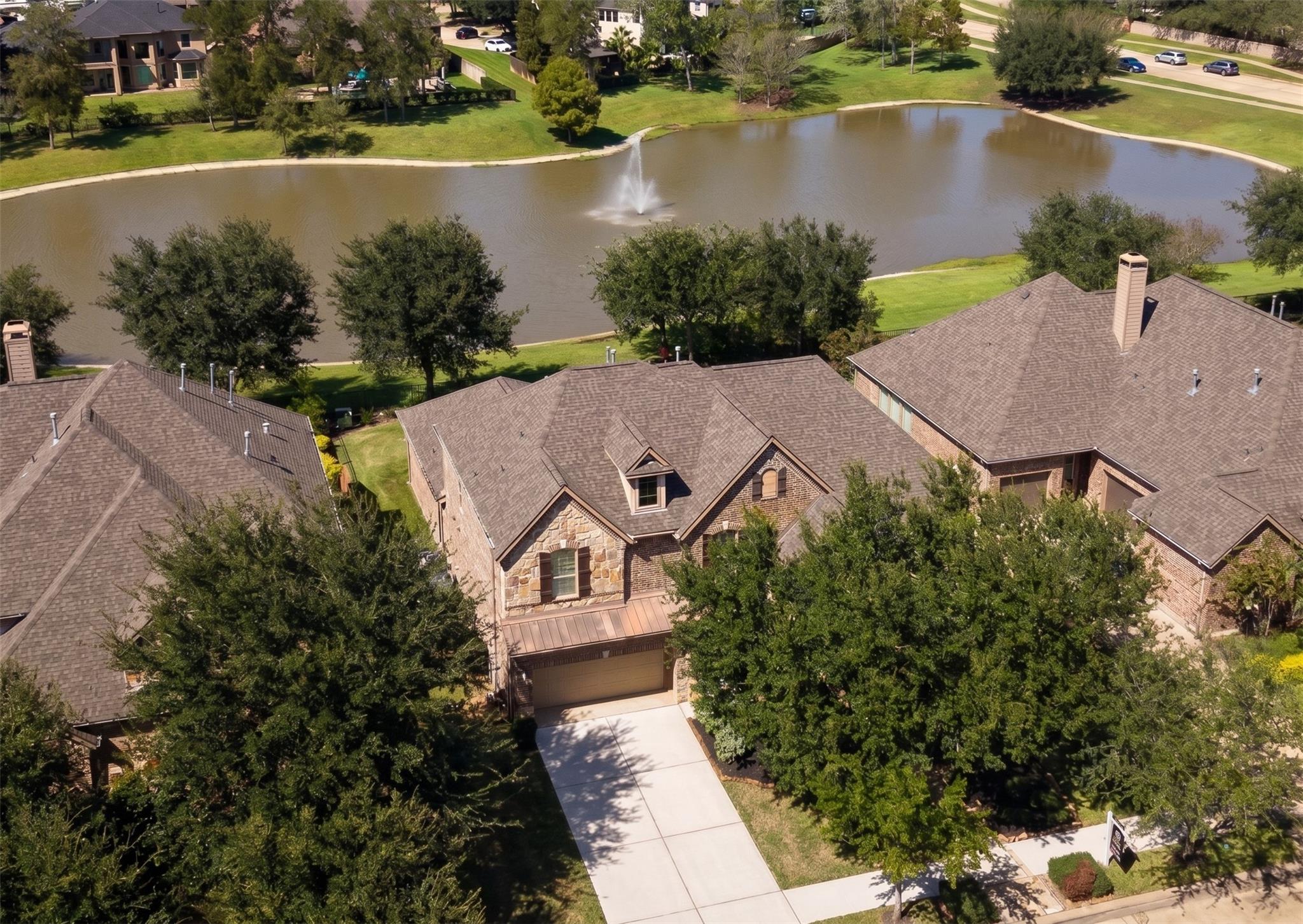 Aerial view of a brick-and-stone home beside a pond with a fountain.