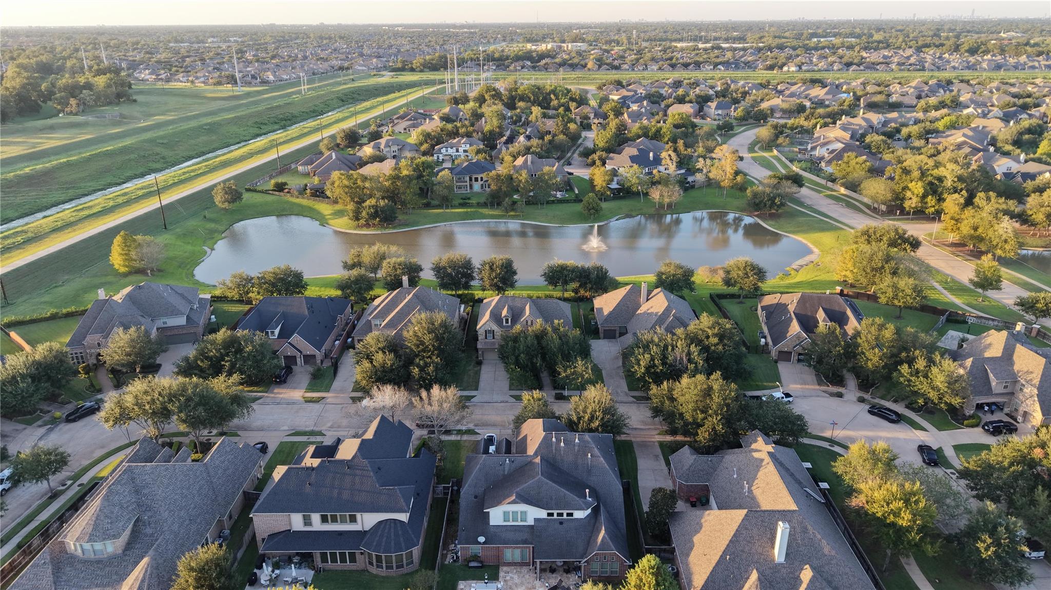 Aerial view of homes around a landscaped pond with a fountain.