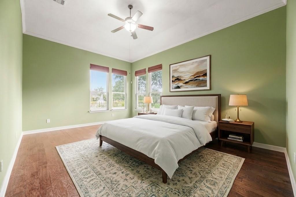Bedroom with pale green walls, a dark wood bed, large windows, and a patterned rug.