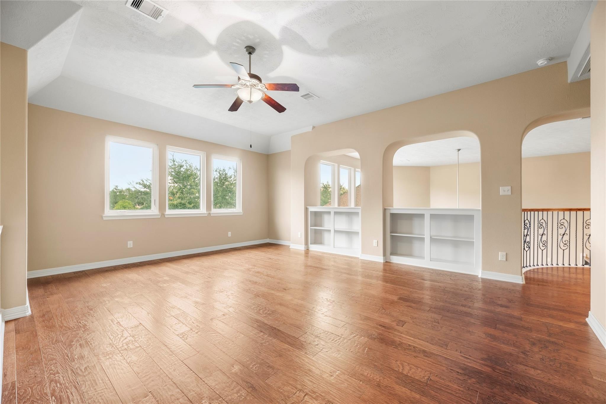 Unfurnished living room with wood floors, built-in shelving, and arched openings.