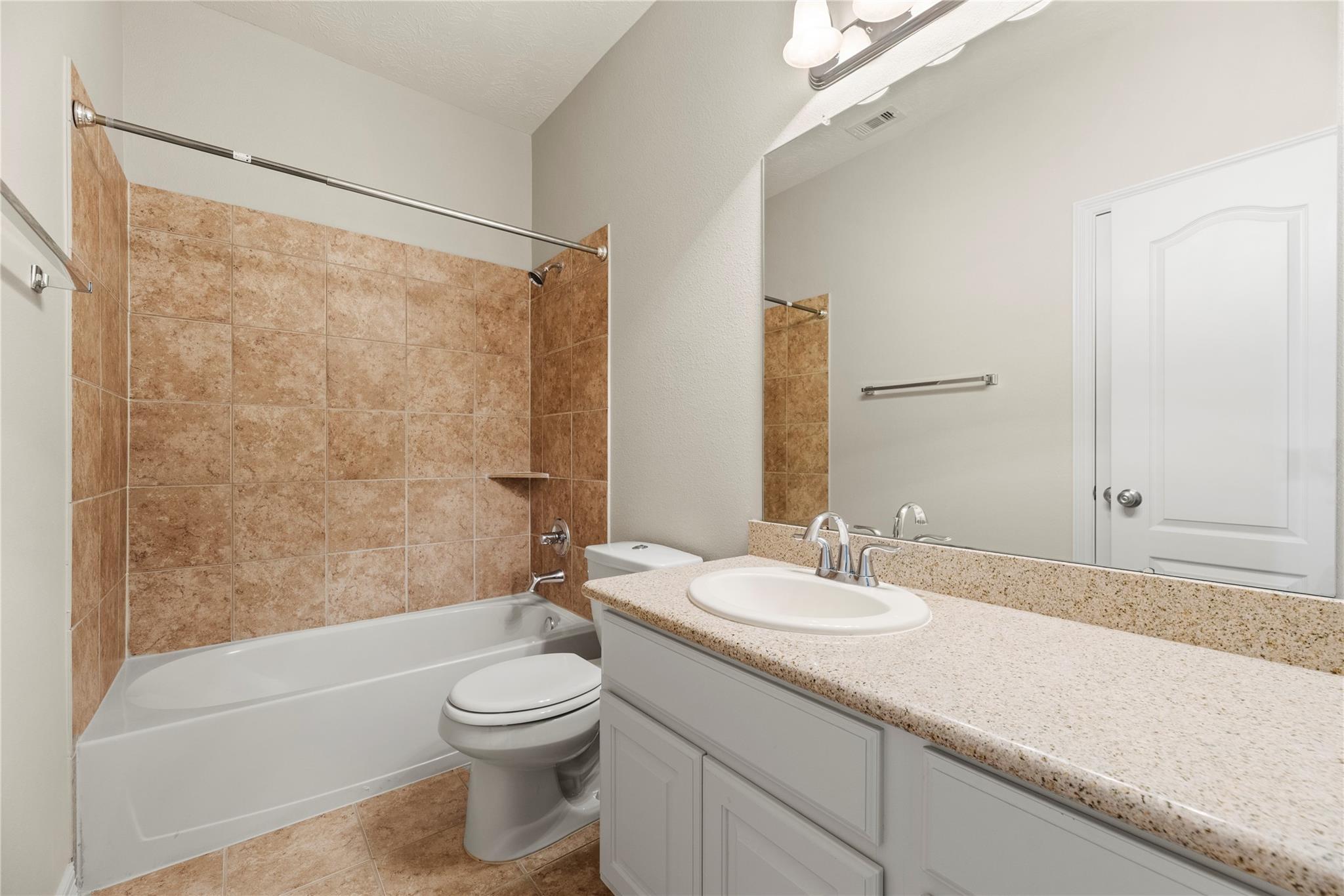 Bathroom with a tan tiled tub and shower beside a granite-topped vanity.
