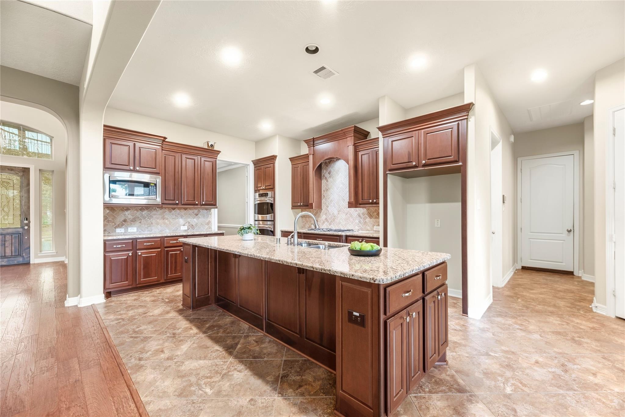 Kitchen with a large granite island, dark wood cabinets, tile backsplash, and double wall ovens.