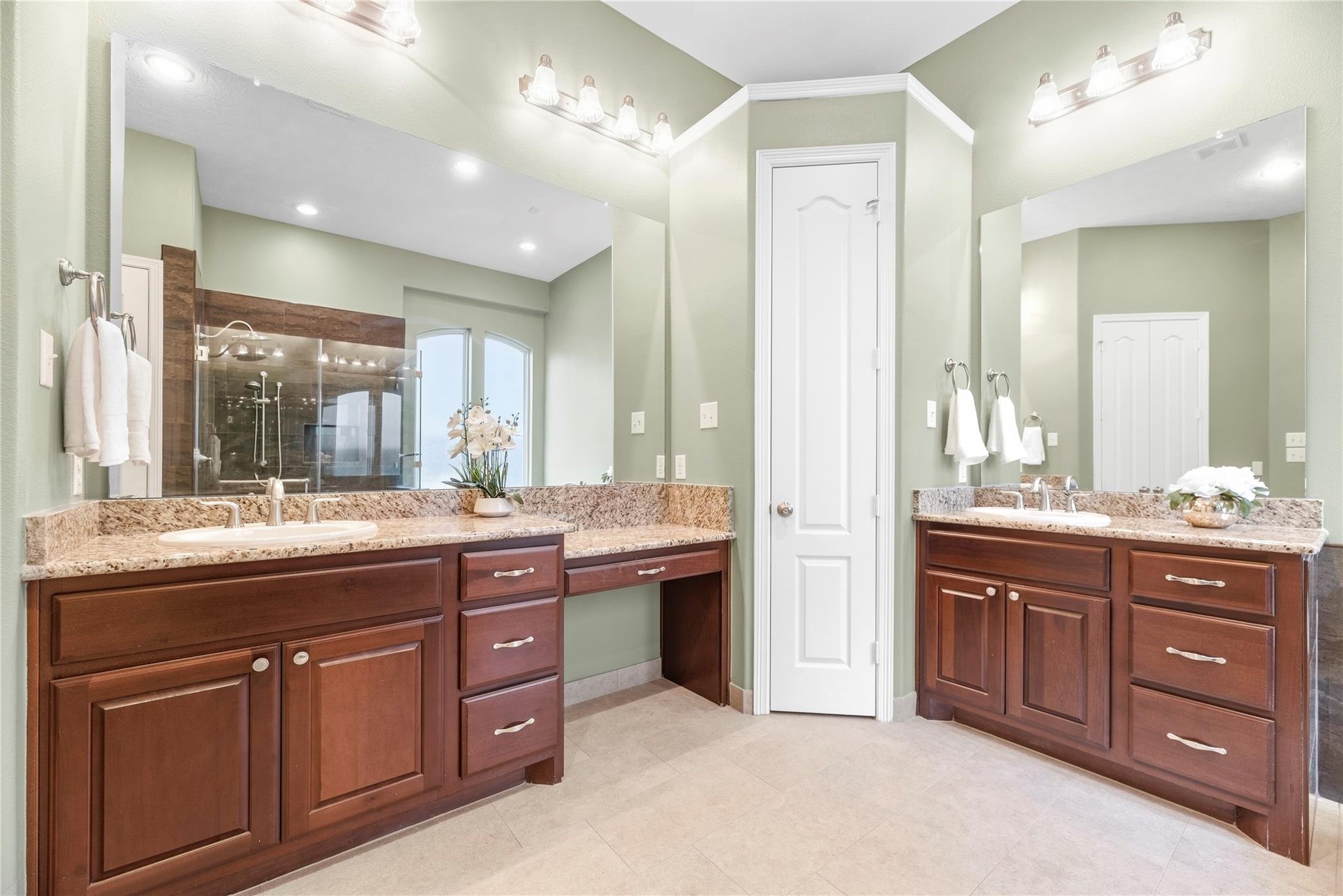 Primary bathroom with dual dark wood vanities, granite countertops, and a glass-enclosed shower.