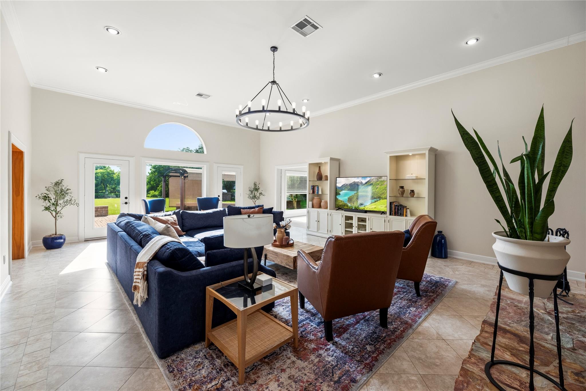 Living room with a navy sectional, leather chairs, circular chandelier, and arched window overlooking the backyard.