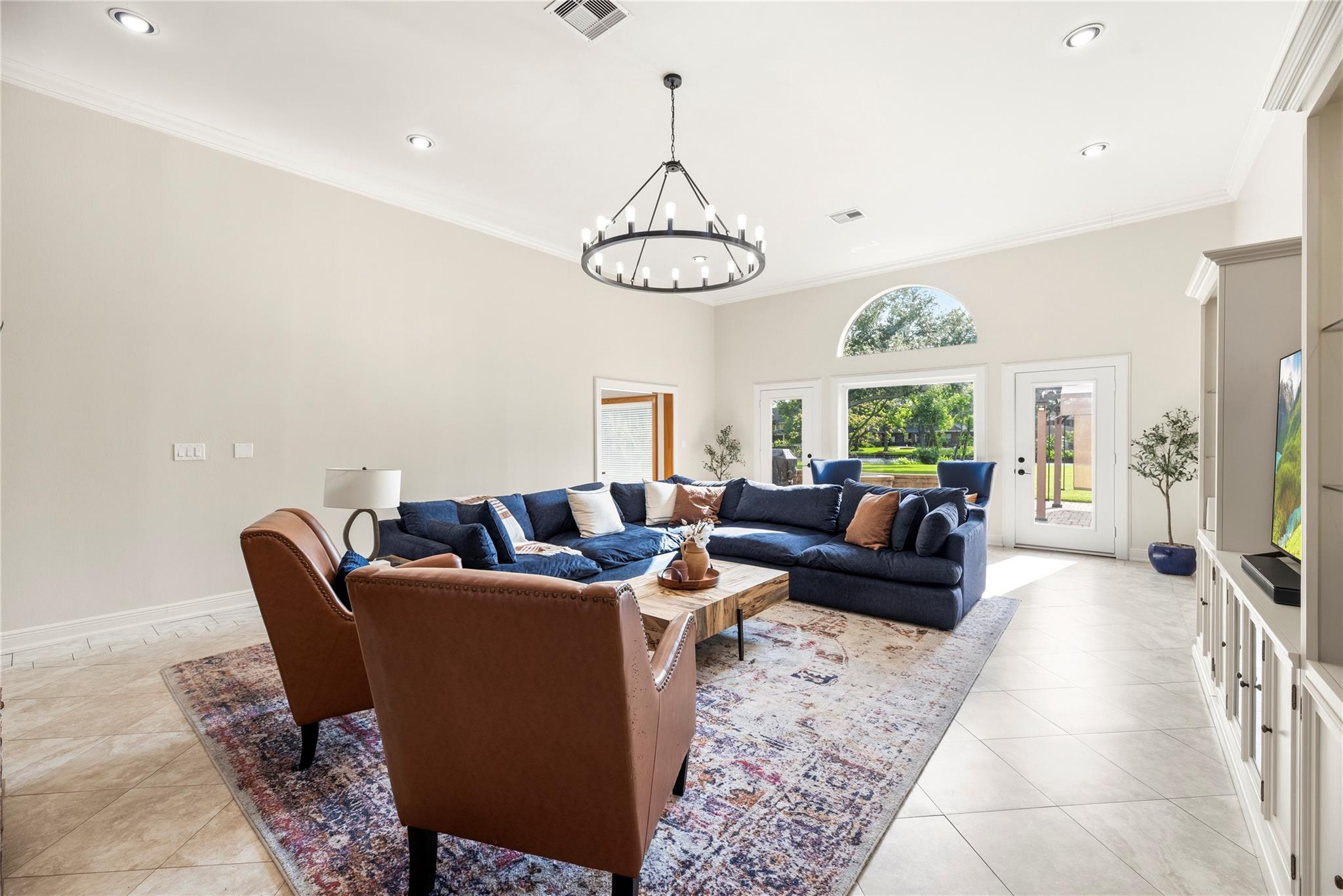Furnished living room with a navy sectional, leather chairs, and large windows overlooking the backyard.