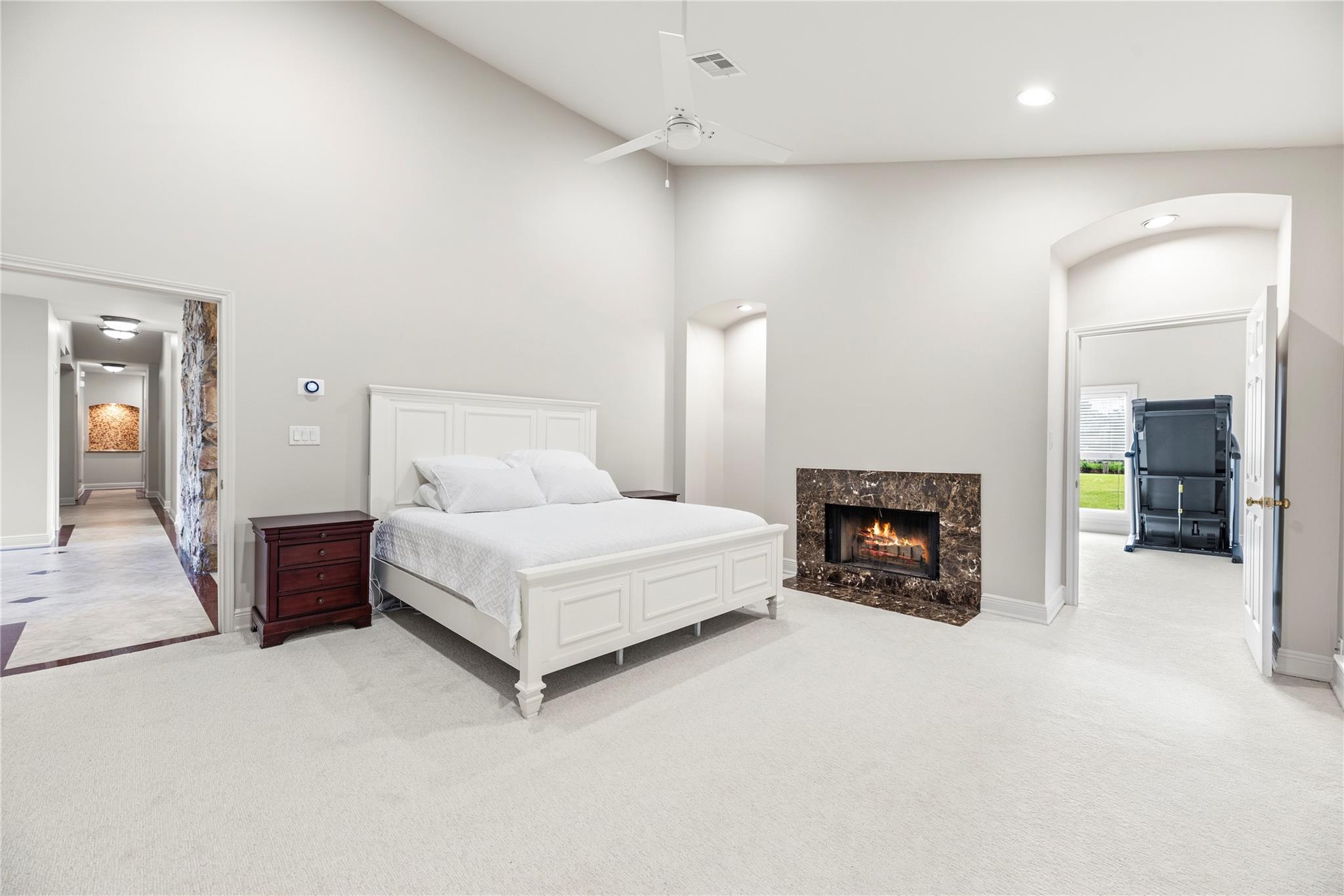 Bedroom with a white bed, vaulted ceiling, and lit marble fireplace