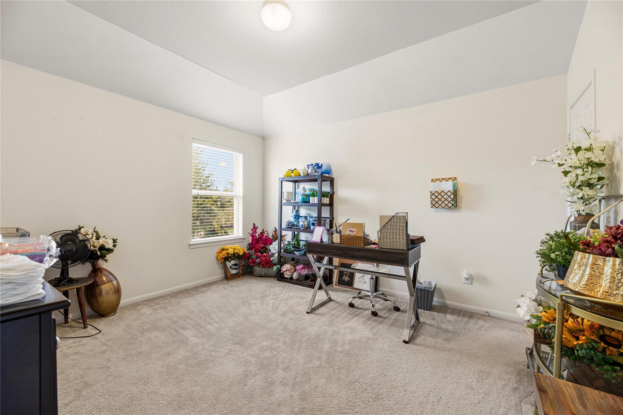 Home office with a desk, rolling chair, shelving, and colorful floral arrangements.
