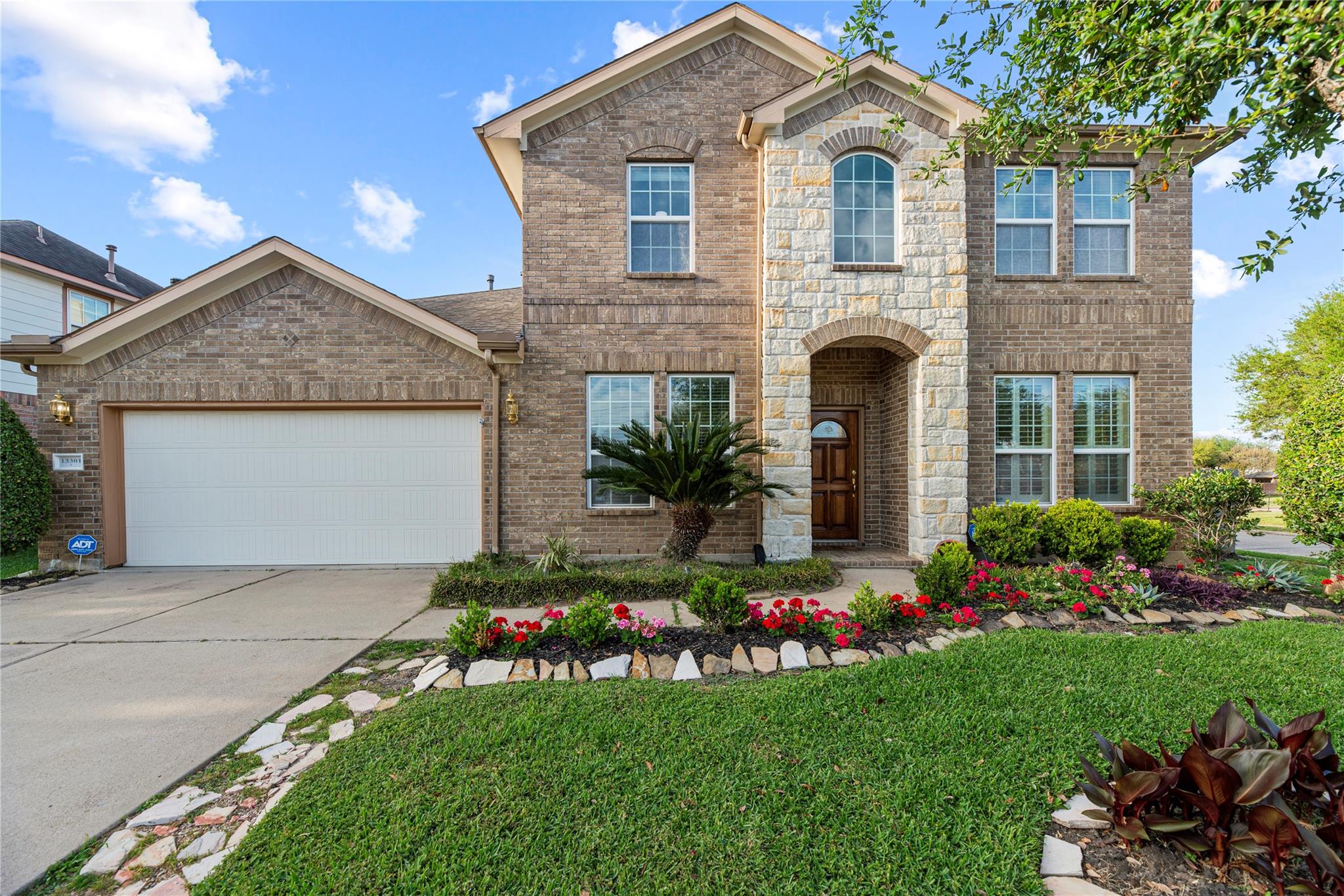 Two-story brick home with a stone entry, two-car garage, and colorful front garden.
