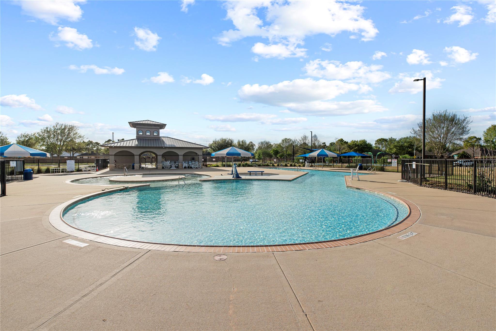 Community swimming pool with a rounded shallow section, shade umbrellas, and a pavilion.