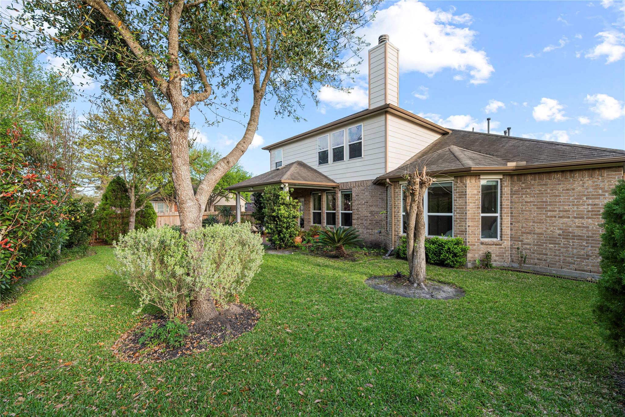 Rear of a two-story brick-and-siding home, framed by mature trees and a landscaped lawn.