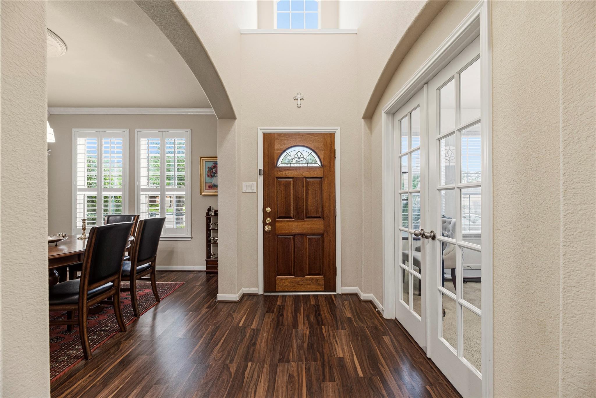 Entryway with a wood front door, tall ceiling, and French doors beside the dining area.