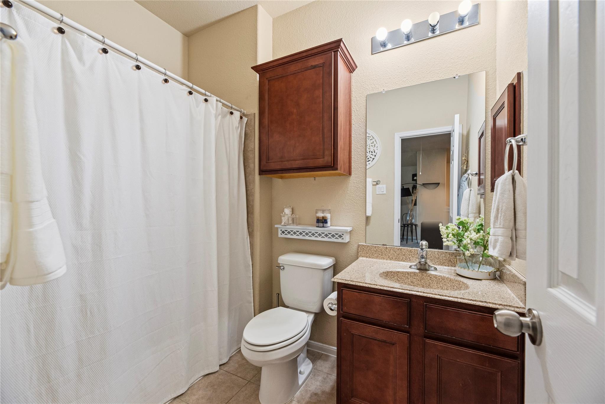 Bathroom with dark wood vanity and cabinet, speckled countertop, and white shower curtain.