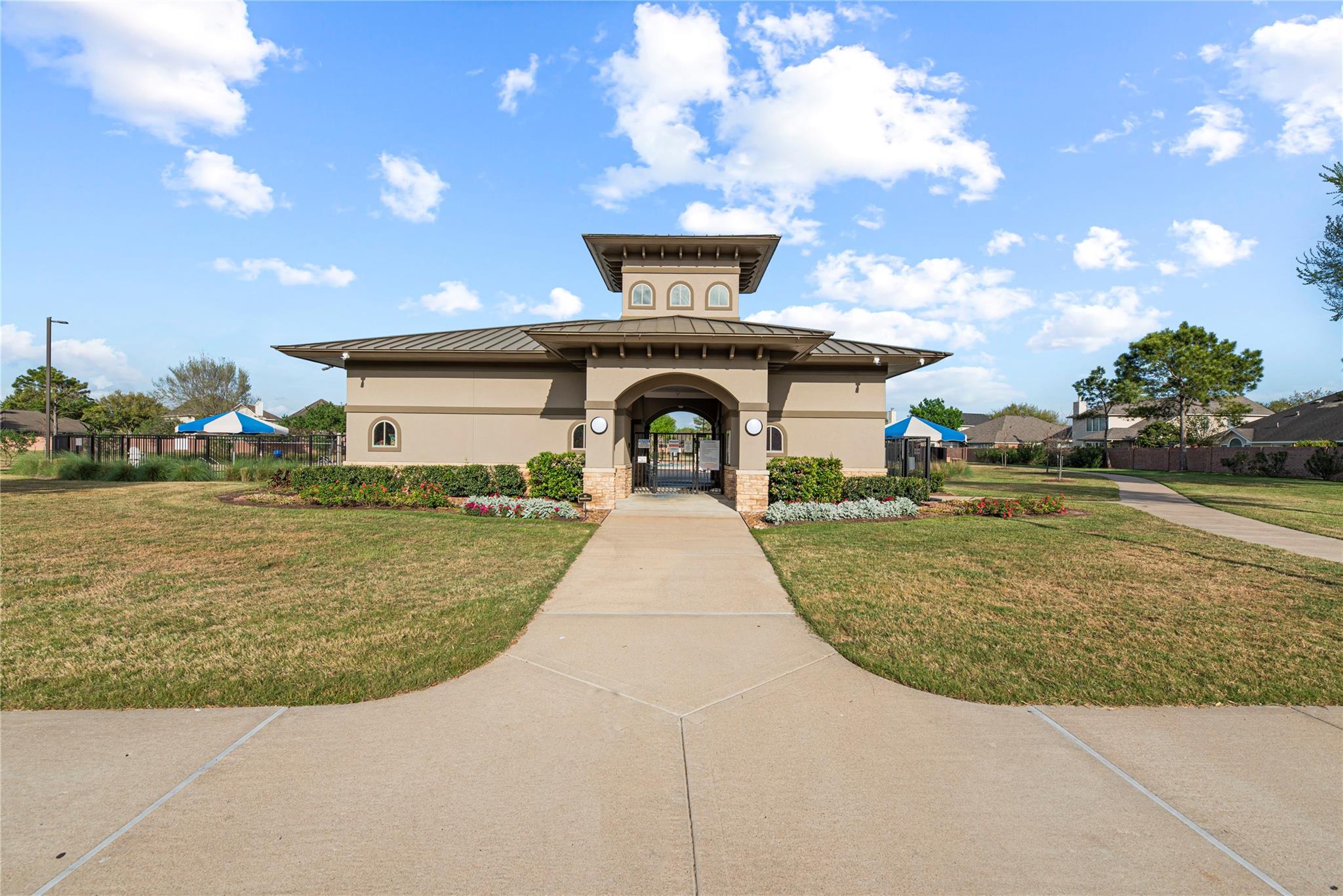 Community entrance pavilion with an arched gate, landscaped flower beds, and a walkway.
