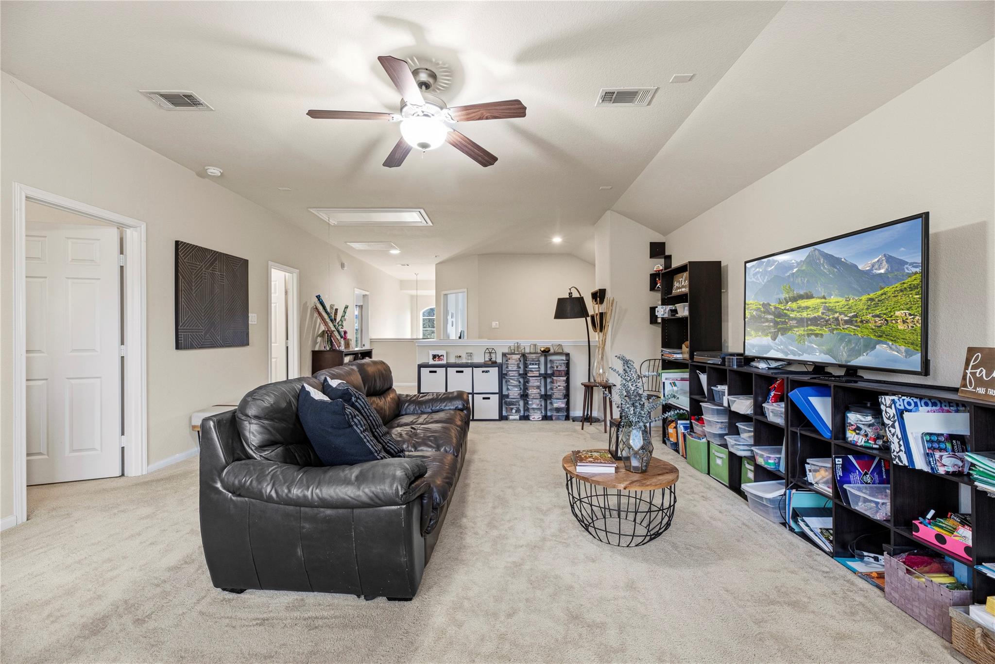 Furnished media room with a black leather sofa, large television, and toy-filled shelving.