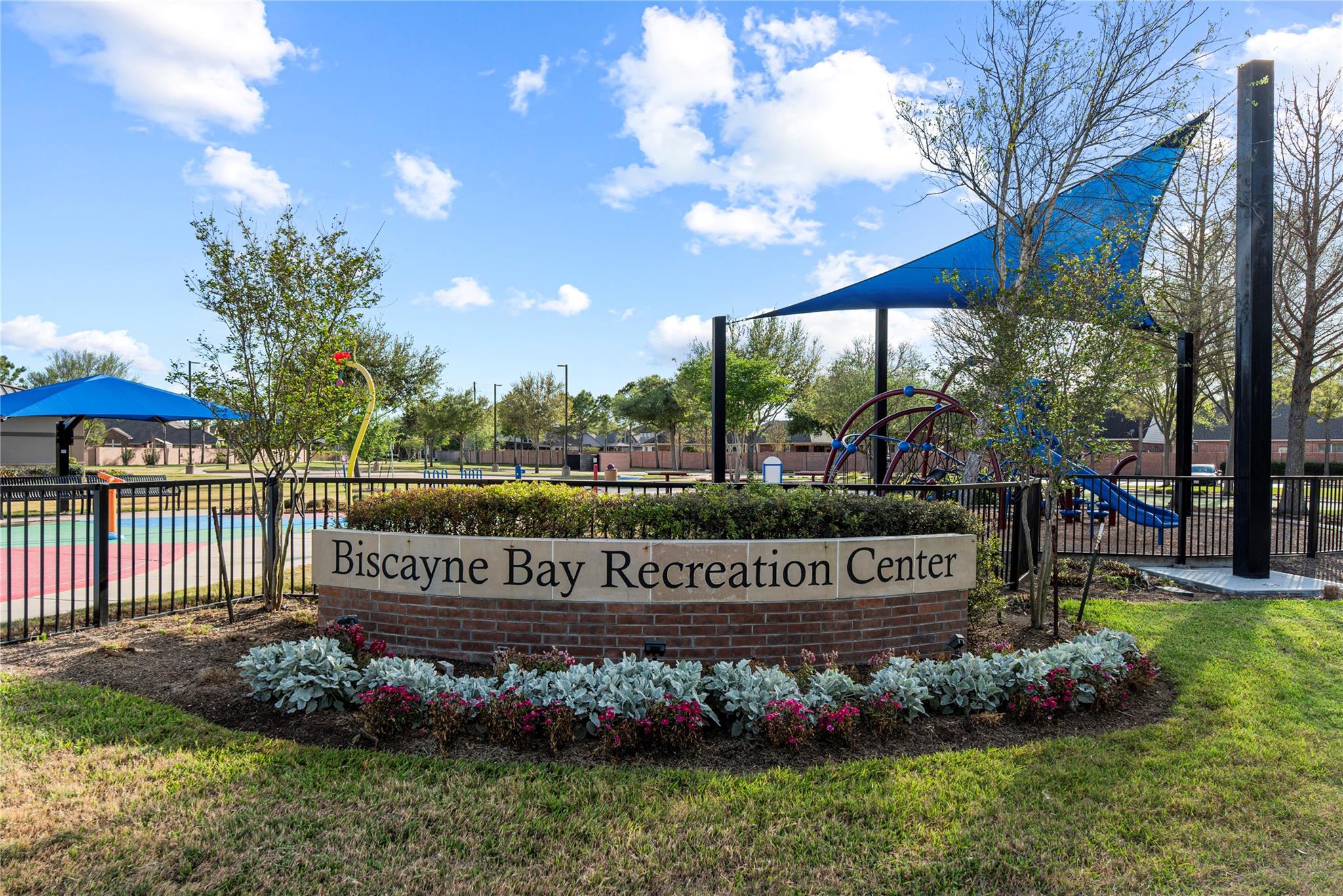 Biscayne Bay Recreation Center sign in front of a fenced playground with blue shade canopies.