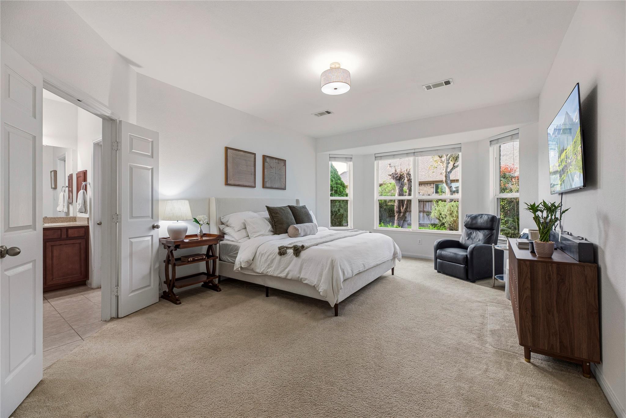 Staged bedroom with a large bed, broad windows, and an open doorway to the en-suite bathroom.