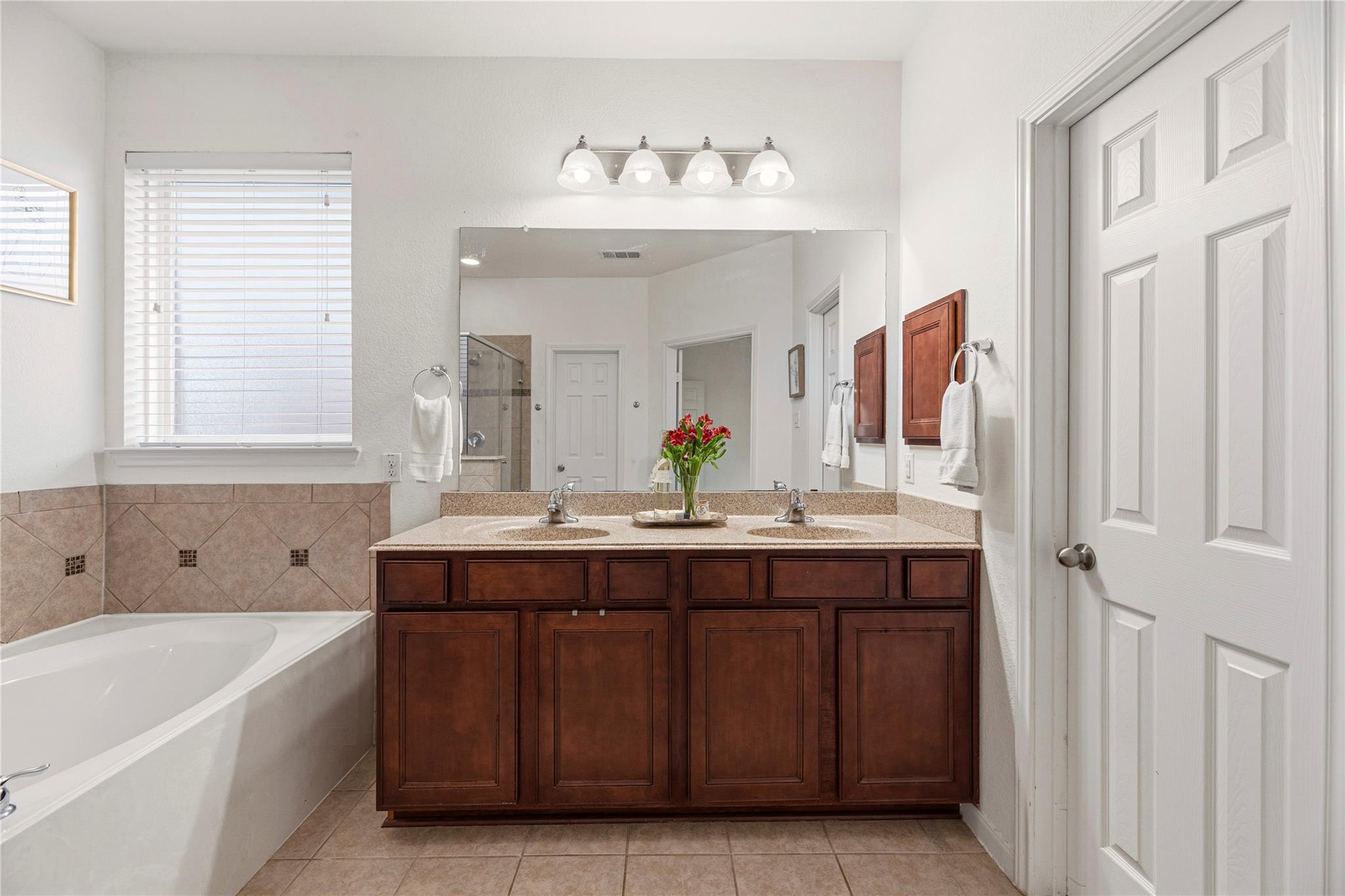 Bathroom with a double-sink dark wood vanity, large mirror, and white soaking tub.