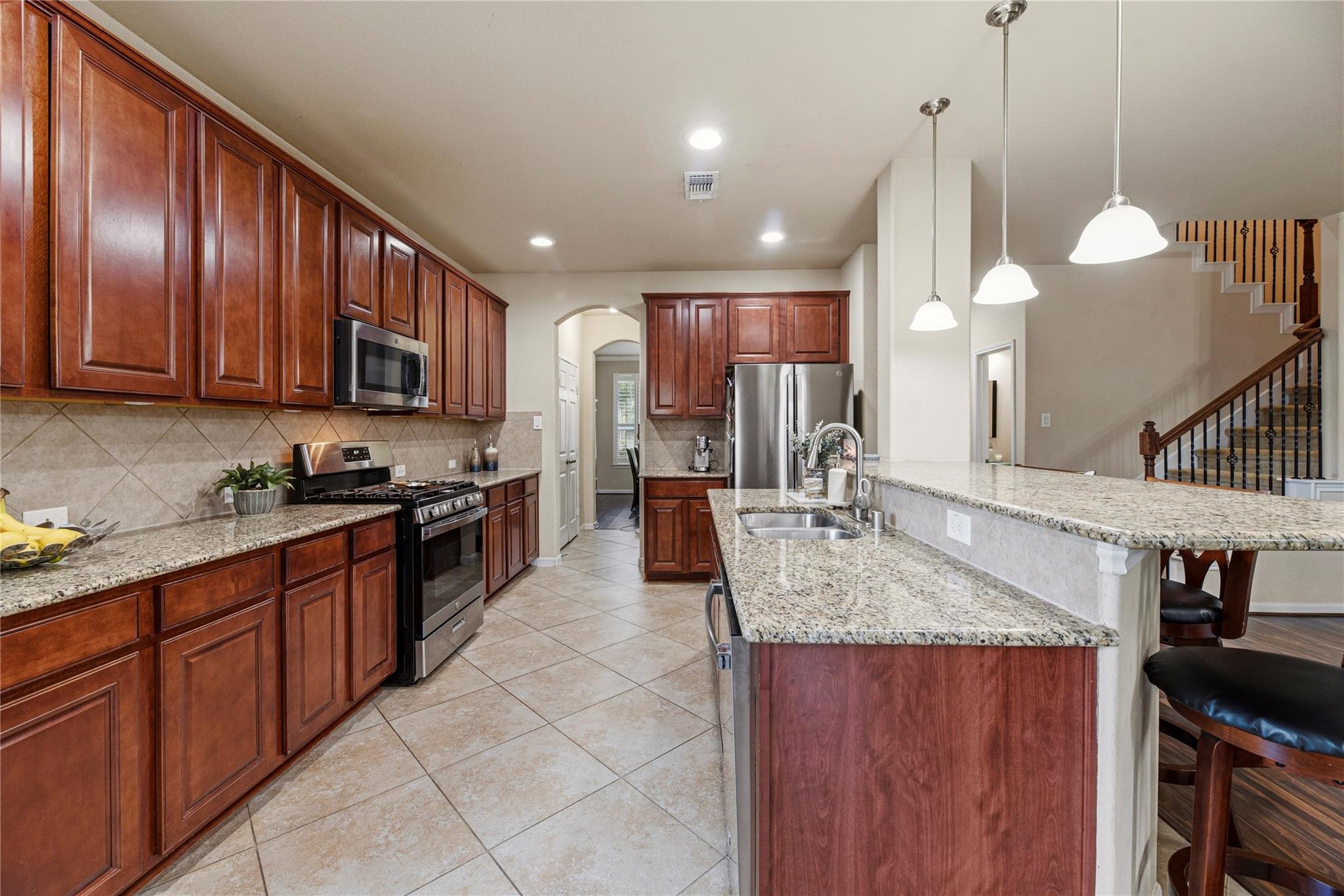 Kitchen with rich wood cabinets, granite island, stainless steel appliances, and pendant lights.