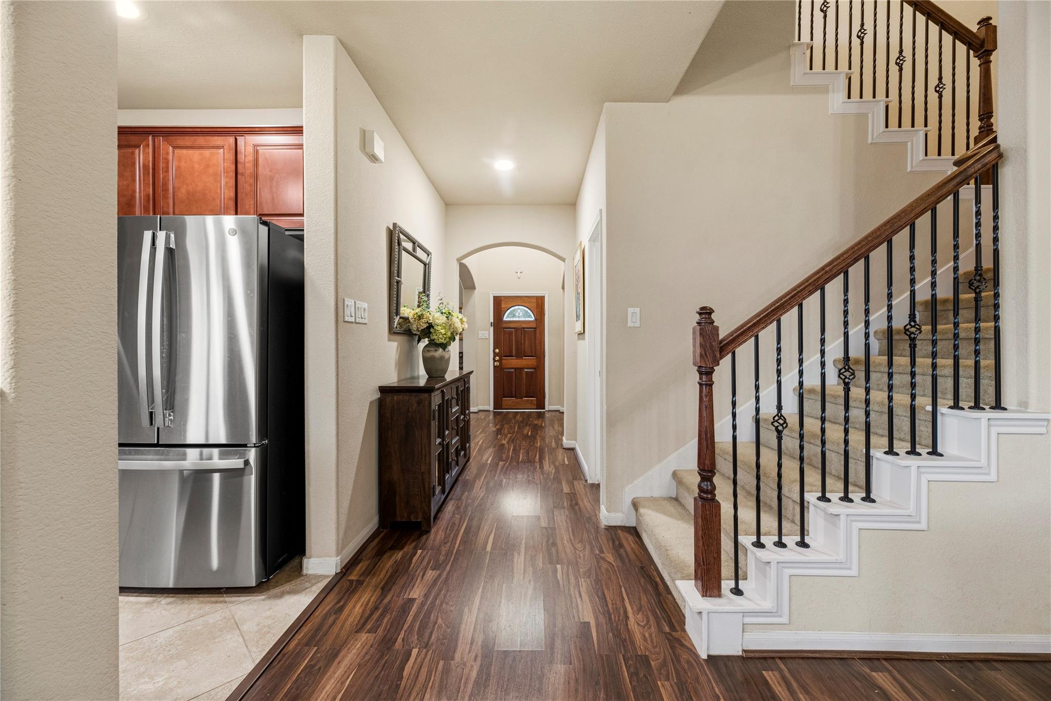 Entry hall with wood floors, a carpeted staircase, and stainless steel refrigerator beside the kitchen.